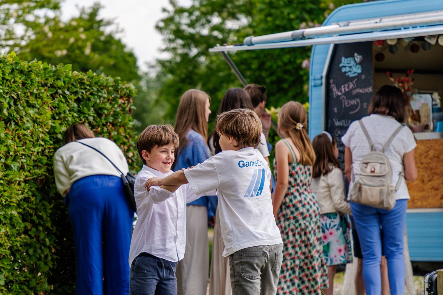 People standing in line at food trucks with blue and white vehicles parked in an outdoor gathering space.