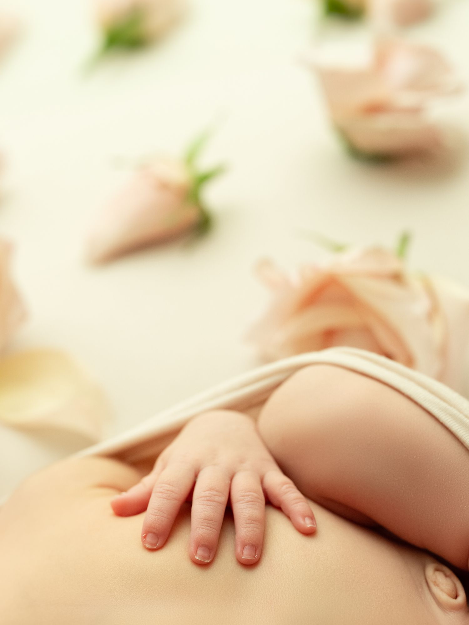 Close-up shot of a tiny baby's hand resting on soft beige fabric showing delicate newborn fingers and creamy skin texture.