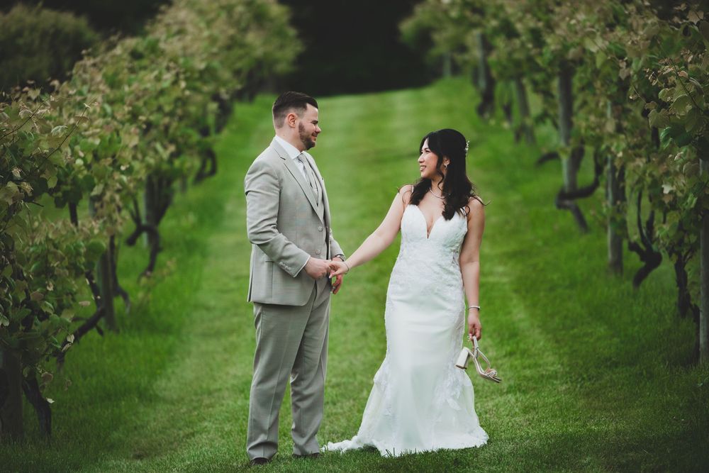 Two people celebrate their wedding day walking through a green apple orchard wearing formal attire.