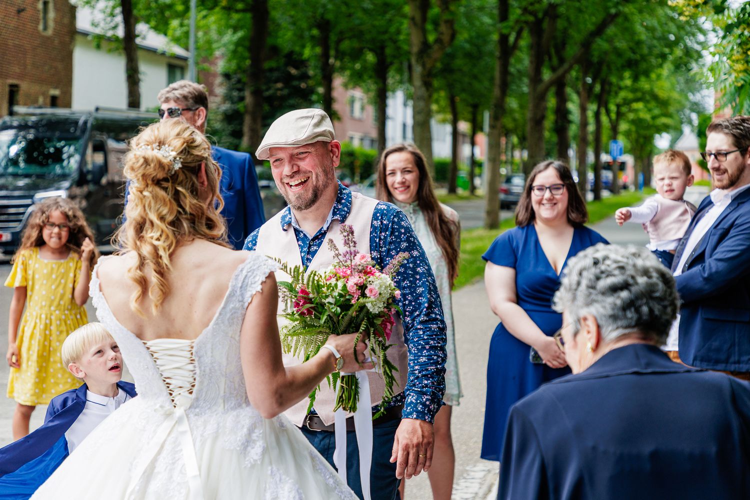 A joyful moment at an outdoor wedding ceremony with guests gathering on a tree-lined street.