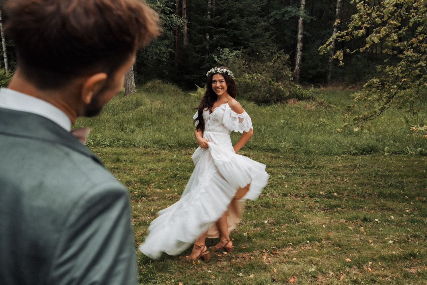 Romantic wedding photo of couple wearing white dress and suit in outdoor forest setting with floral crown.