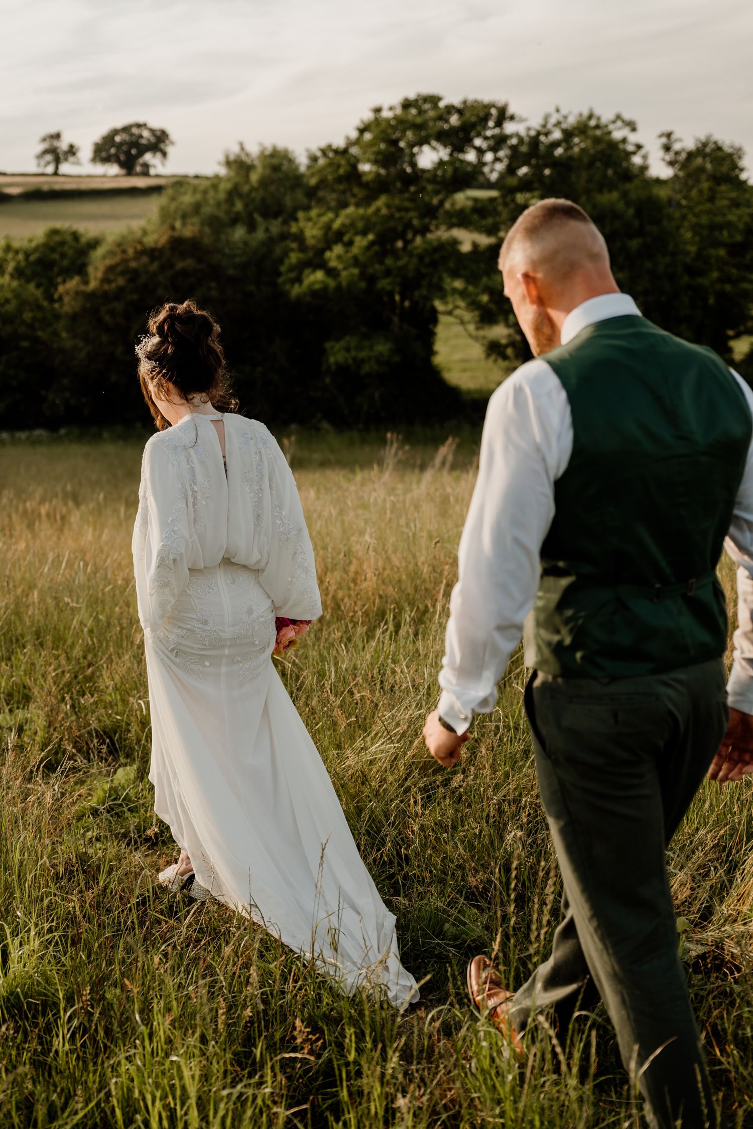 Couple strolling through a meadow with golden light filtering through trees.