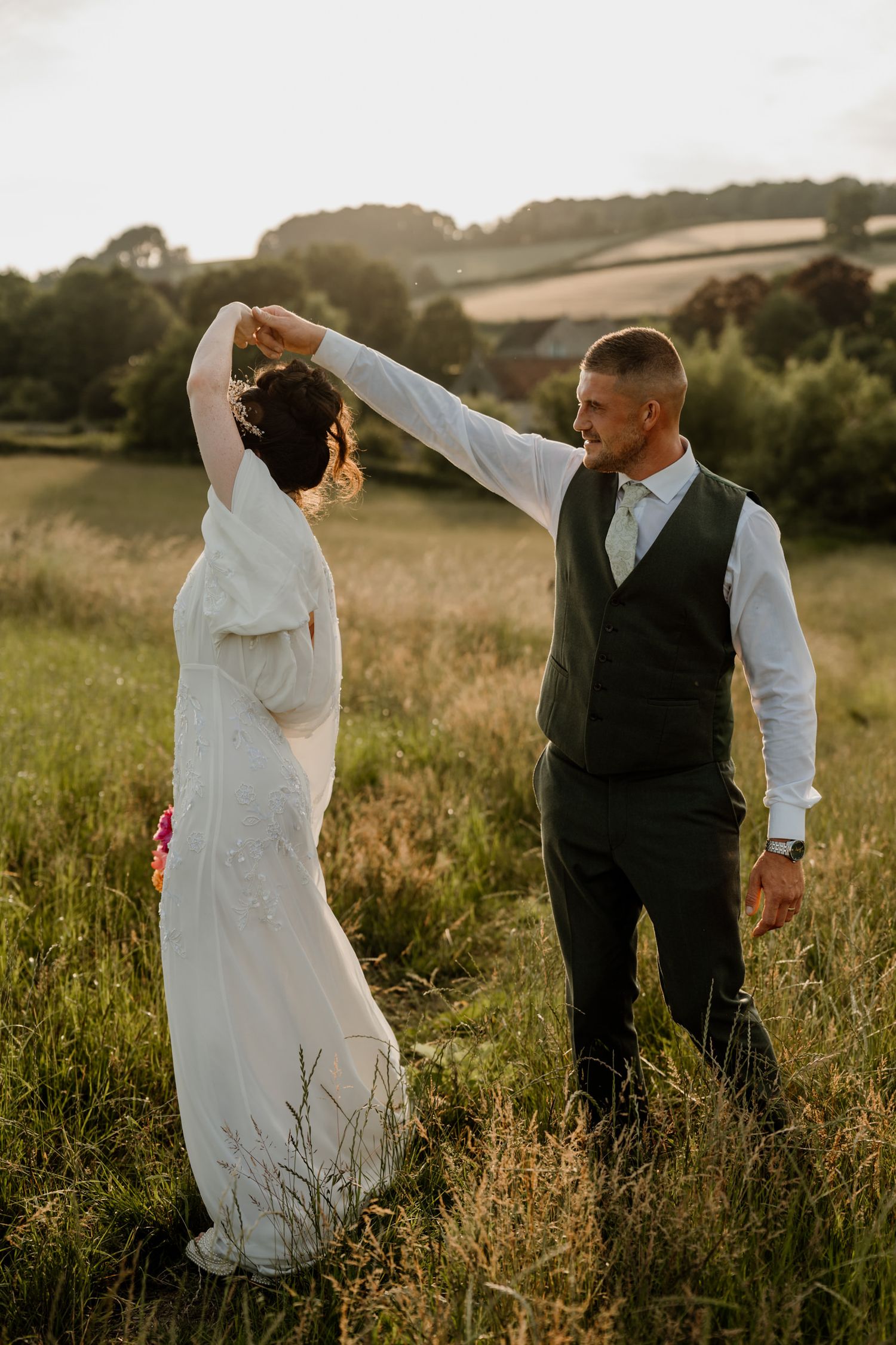 Newlyweds dancing playfully in a summer meadow at golden hour.