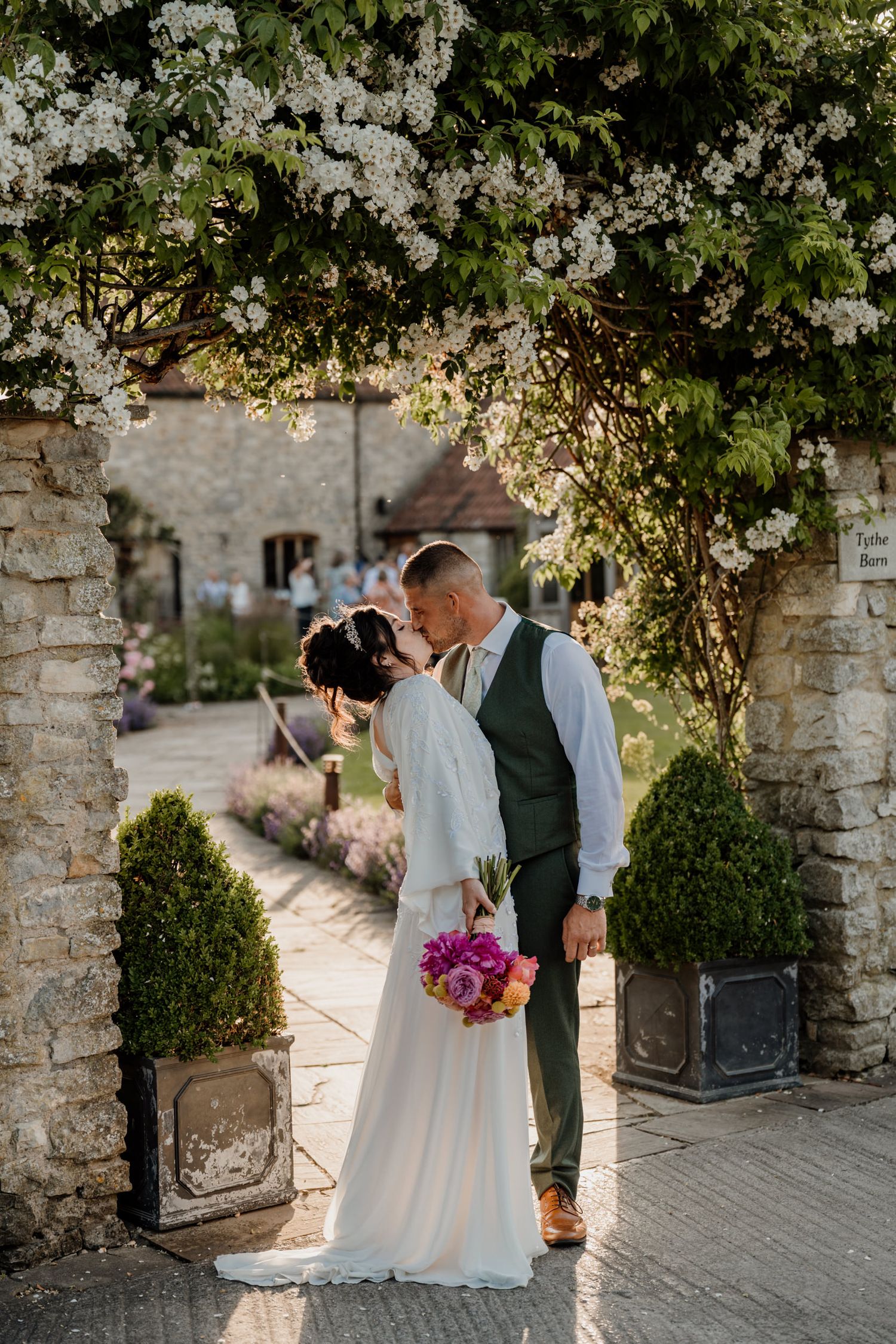 Stone archway decorated with climbing white flowers creates romantic wedding day setting.