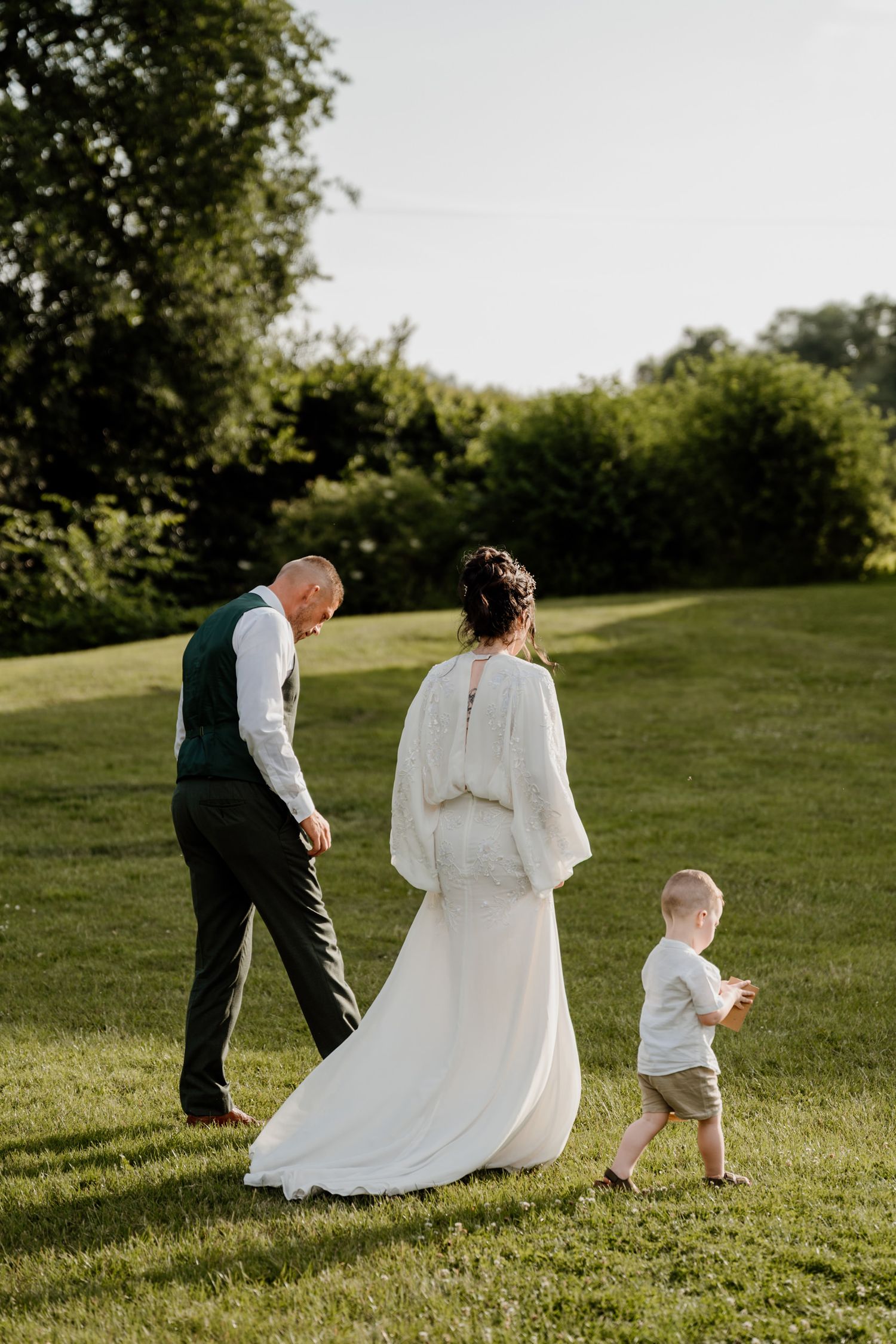 Wedding party walking through sunny green hillside during summer celebration.