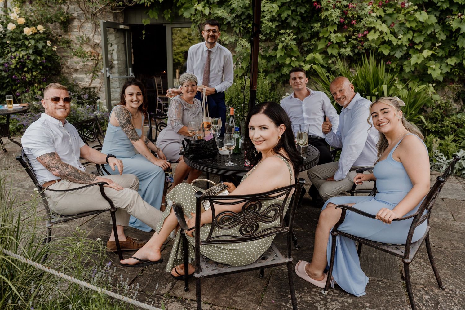 Wedding party relaxes on outdoor benches during a casual reception gathering.