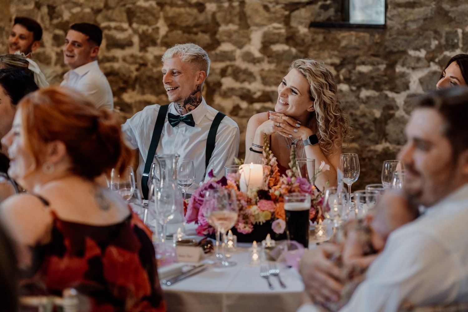 Wedding reception guests enjoy dinner and conversation inside a rustic stone-walled venue.
