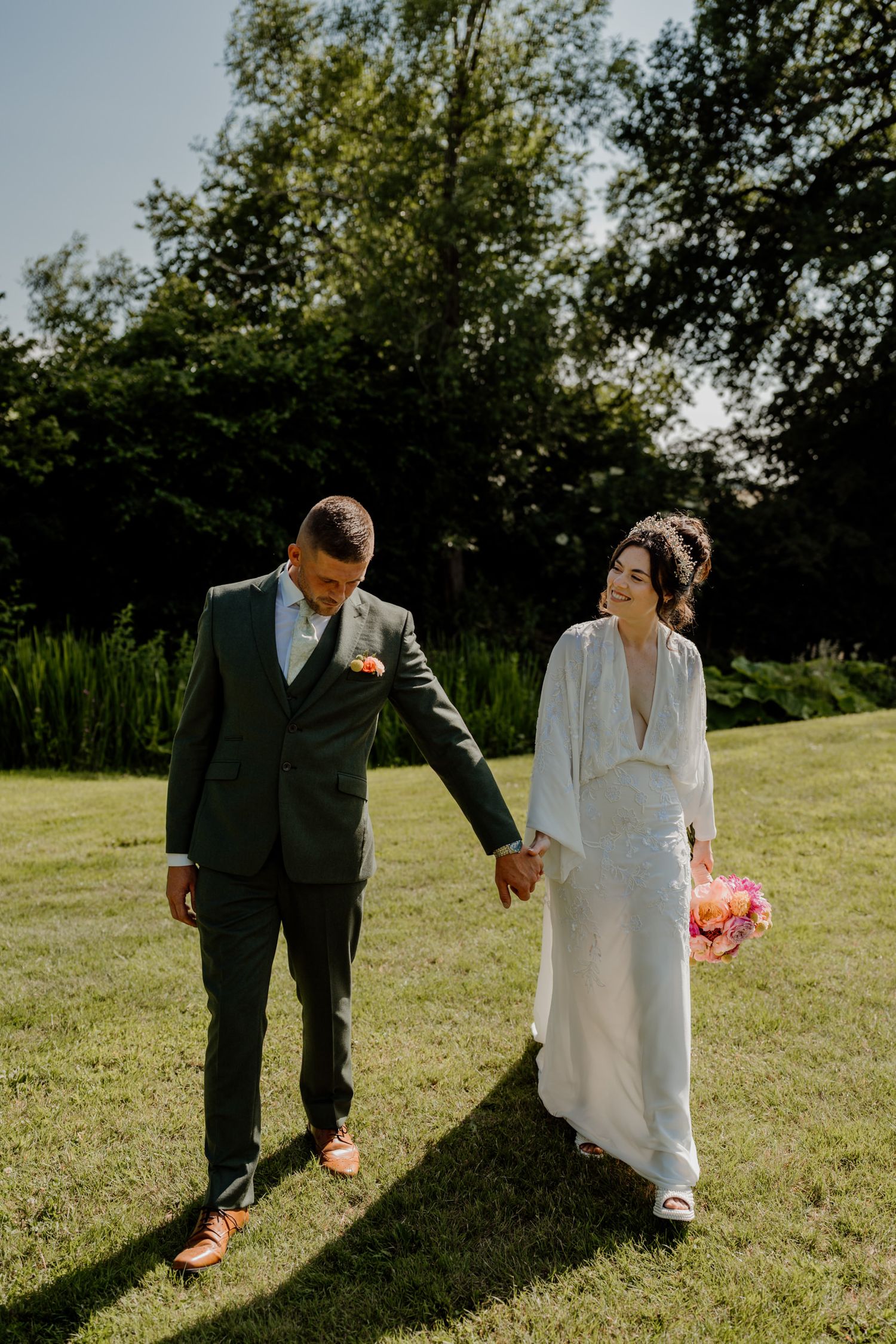 Couple walking hand in hand across a sunlit grassy field casting long shadows.