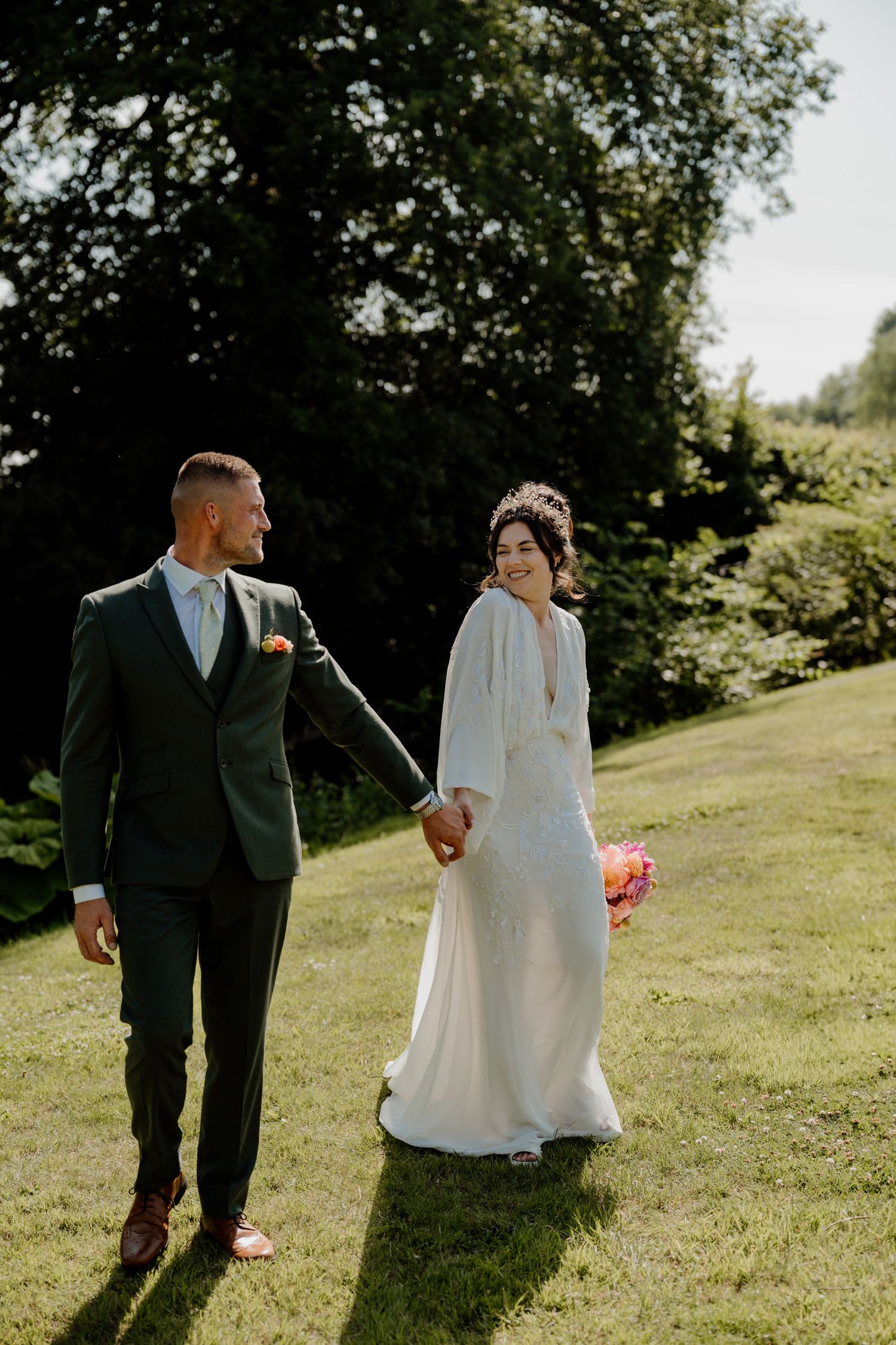 Wedding couple strolling on grassy hillside during golden hour photography session.