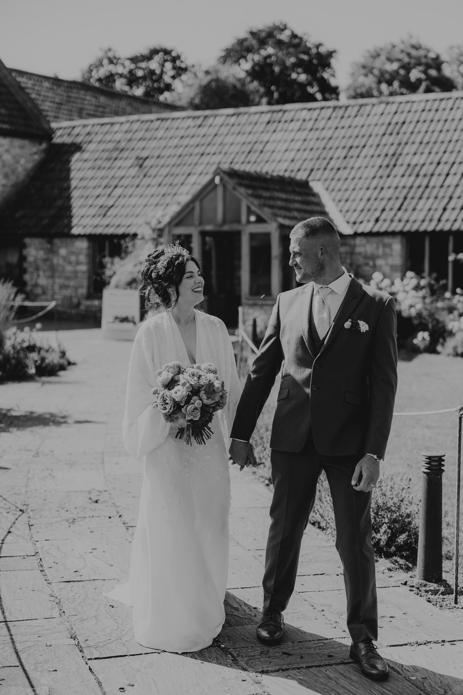 Black and white photo of couple standing near stone buildings with tiled roofs.