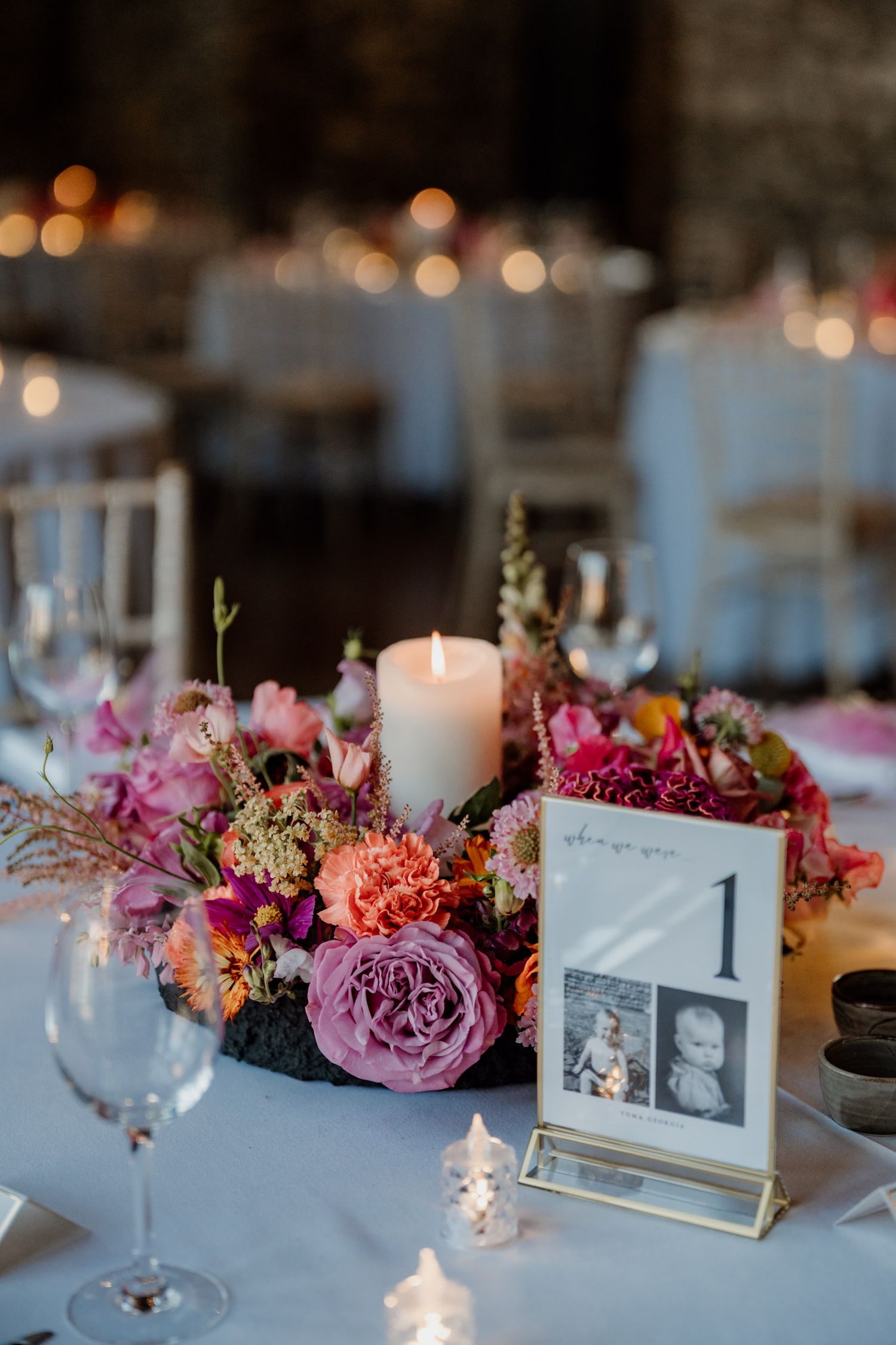 Elegant wedding reception table with pink floral centerpieces, candles and table number displays.
