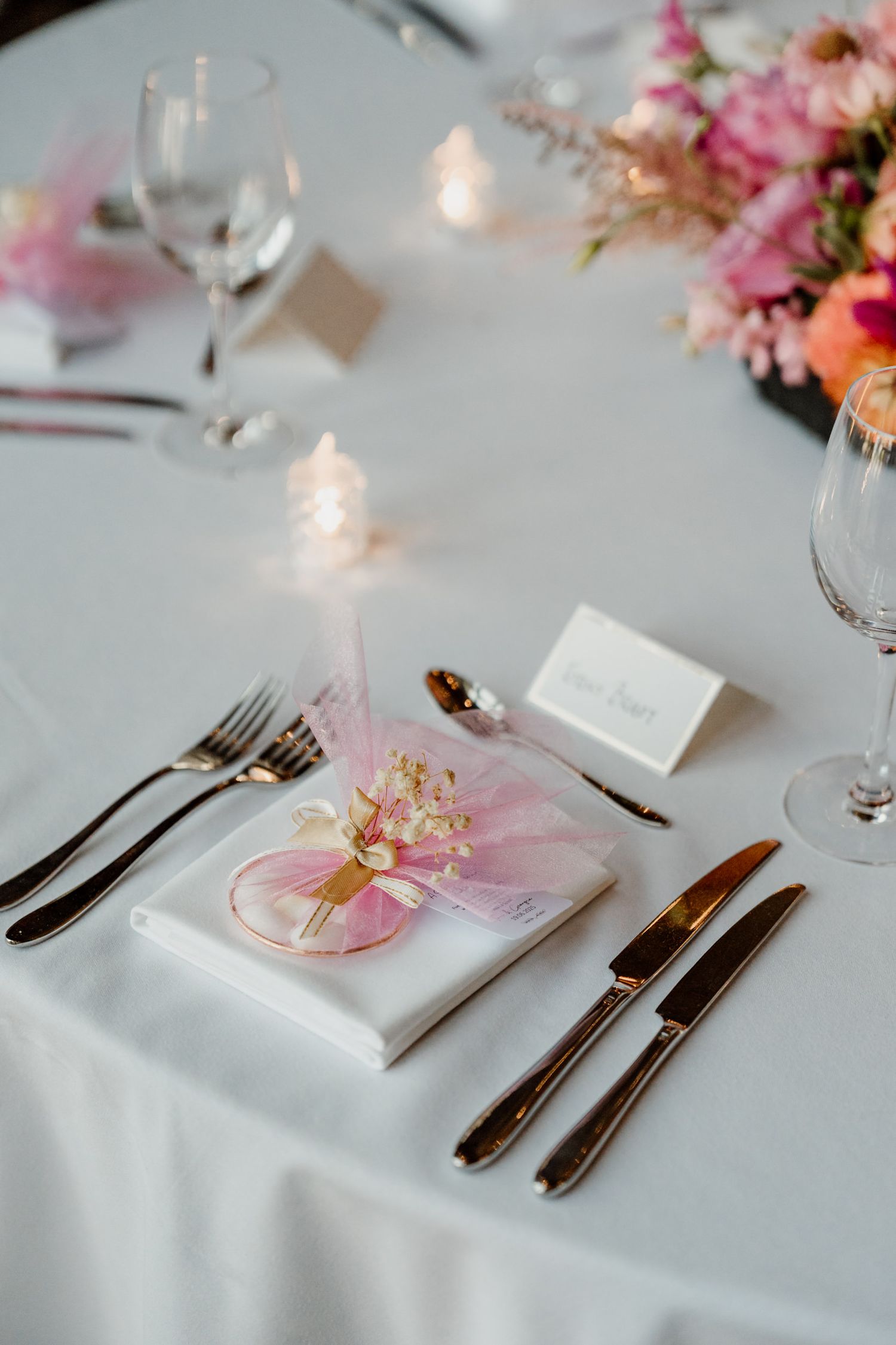 Elegant wedding table setting with pink floral accents and silverware on crisp white linens.
