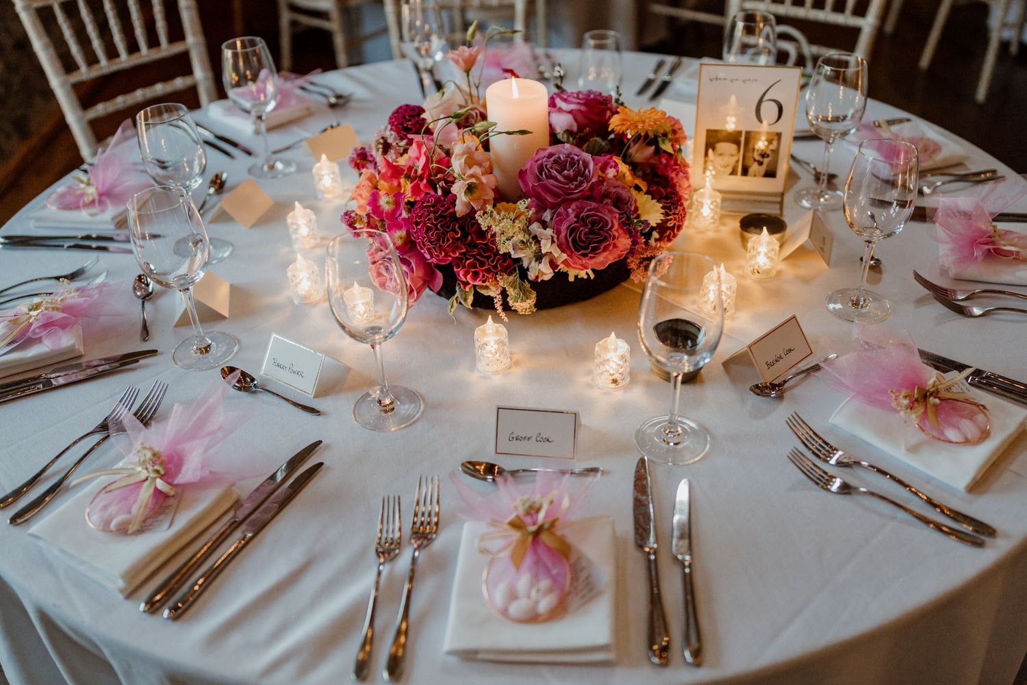 Beautifully decorated round reception tables with pink and burgundy floral centerpieces and glowing candles.