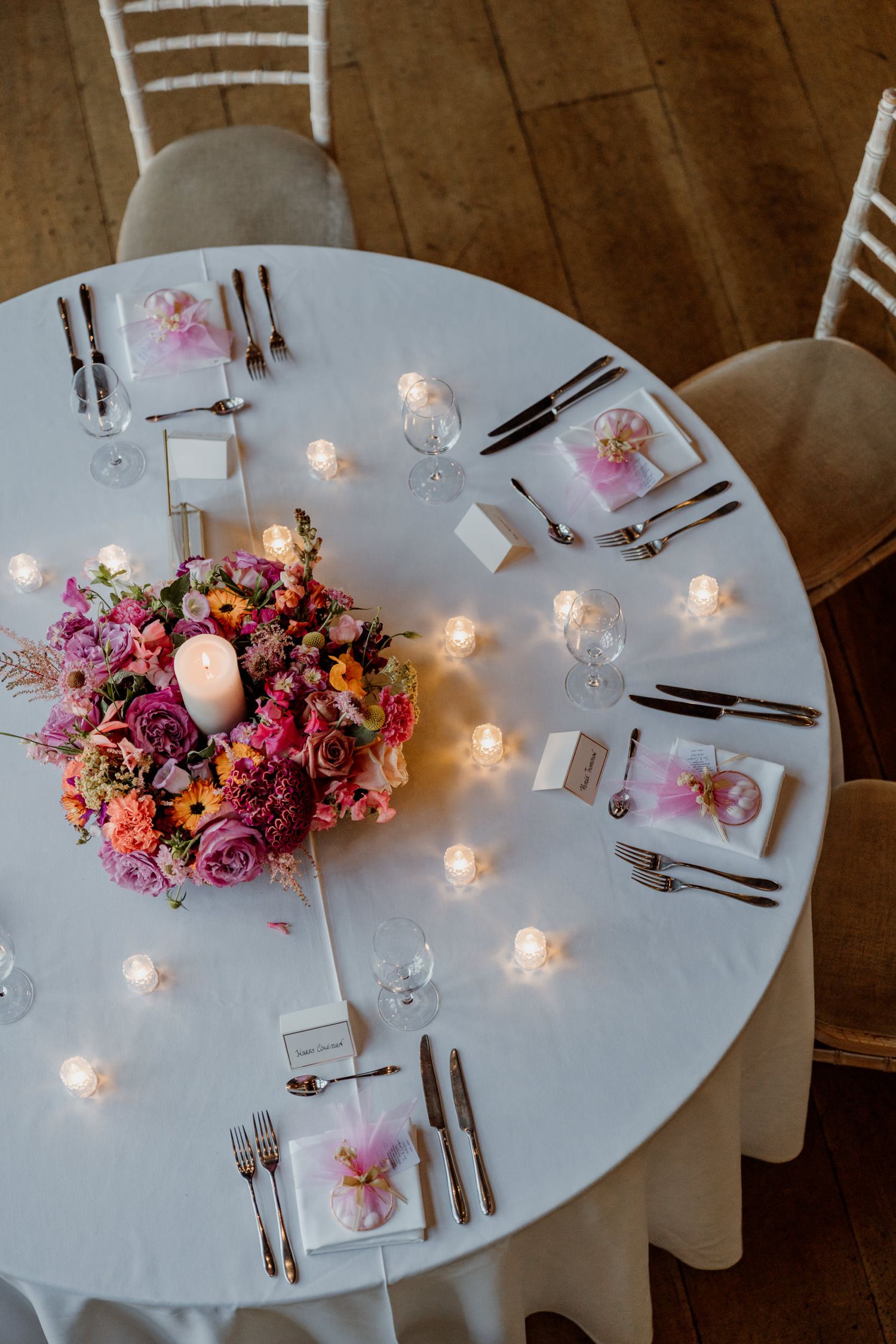 Round reception tables with white linens decorated with pink floral arrangements and glowing candles.