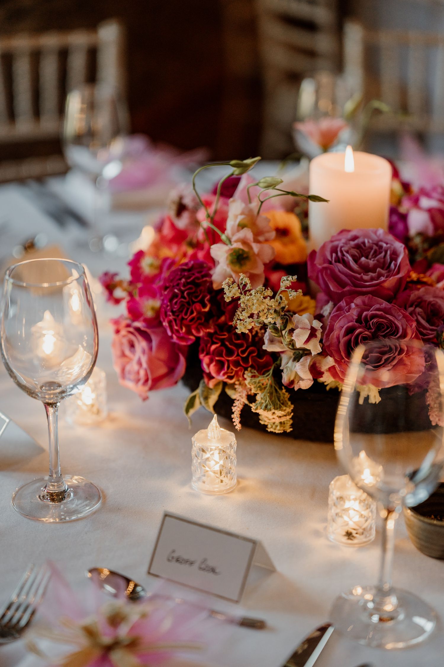 Wedding table settings feature vibrant pink and burgundy floral arrangements with glowing candlelight.