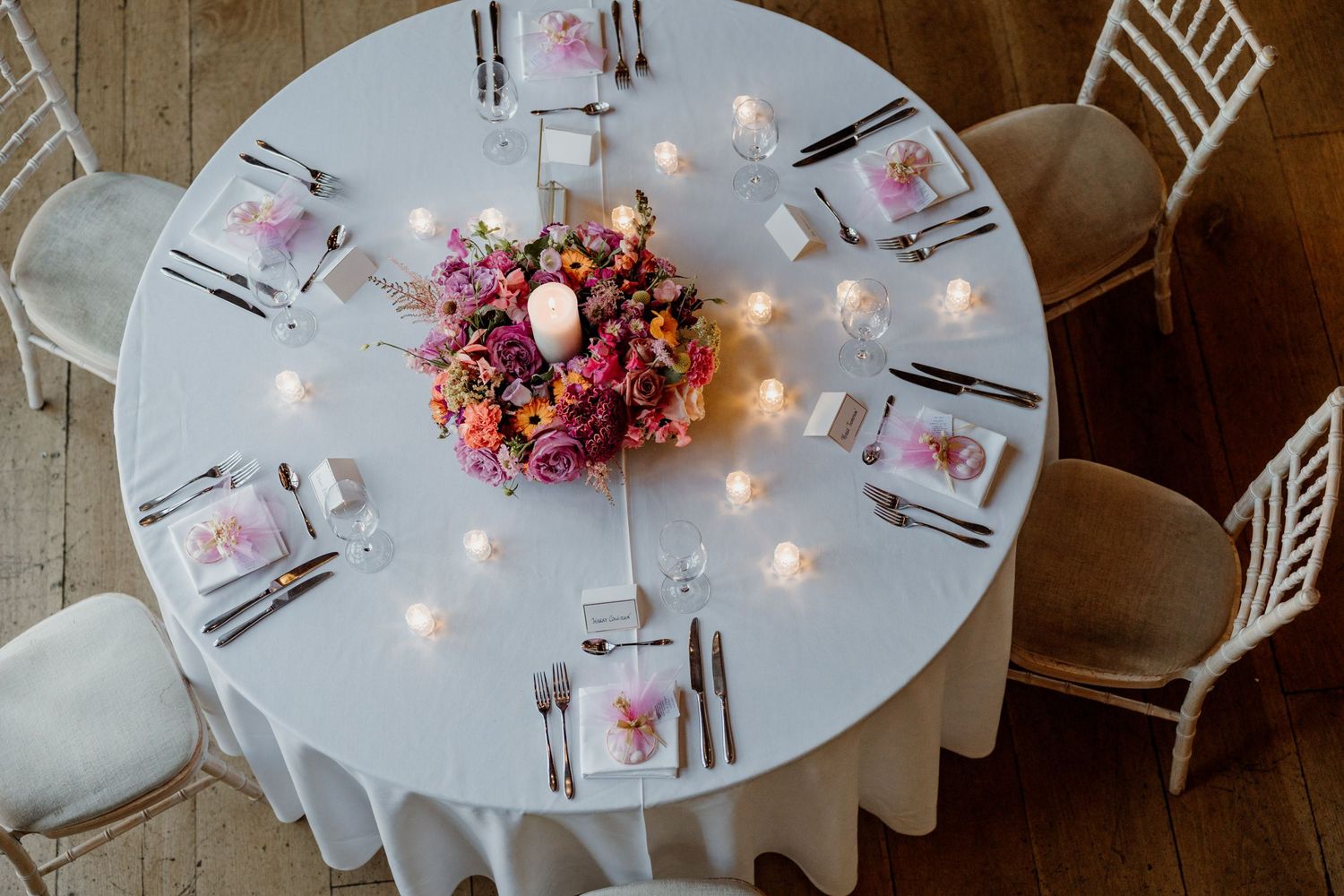 Overhead view of elegant wedding reception tables with white chairs and pink floral centerpieces illuminated by string lights.