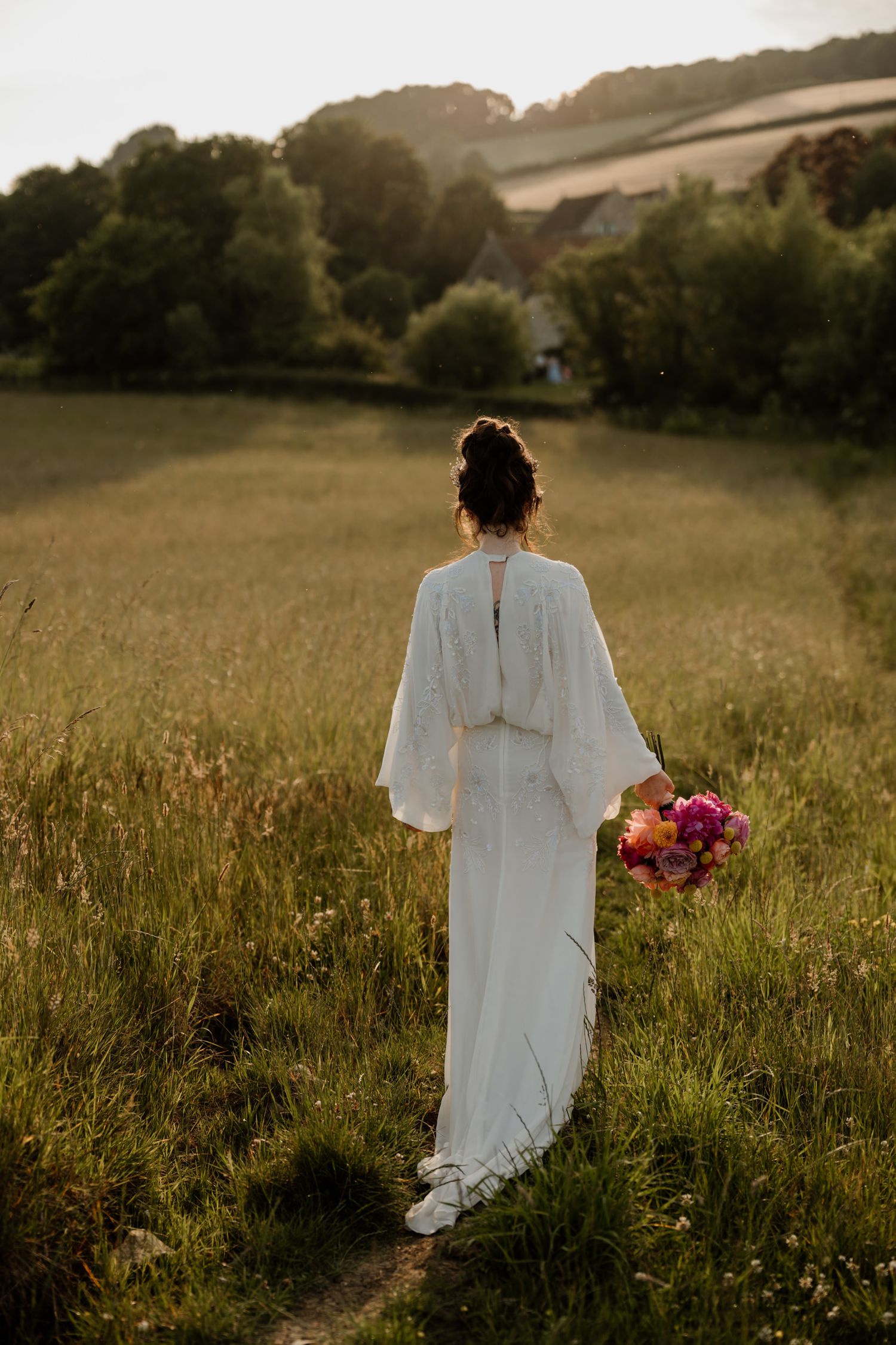 Wedding dress silhouette against a serene countryside landscape at golden hour at Priston Mill in Bath.