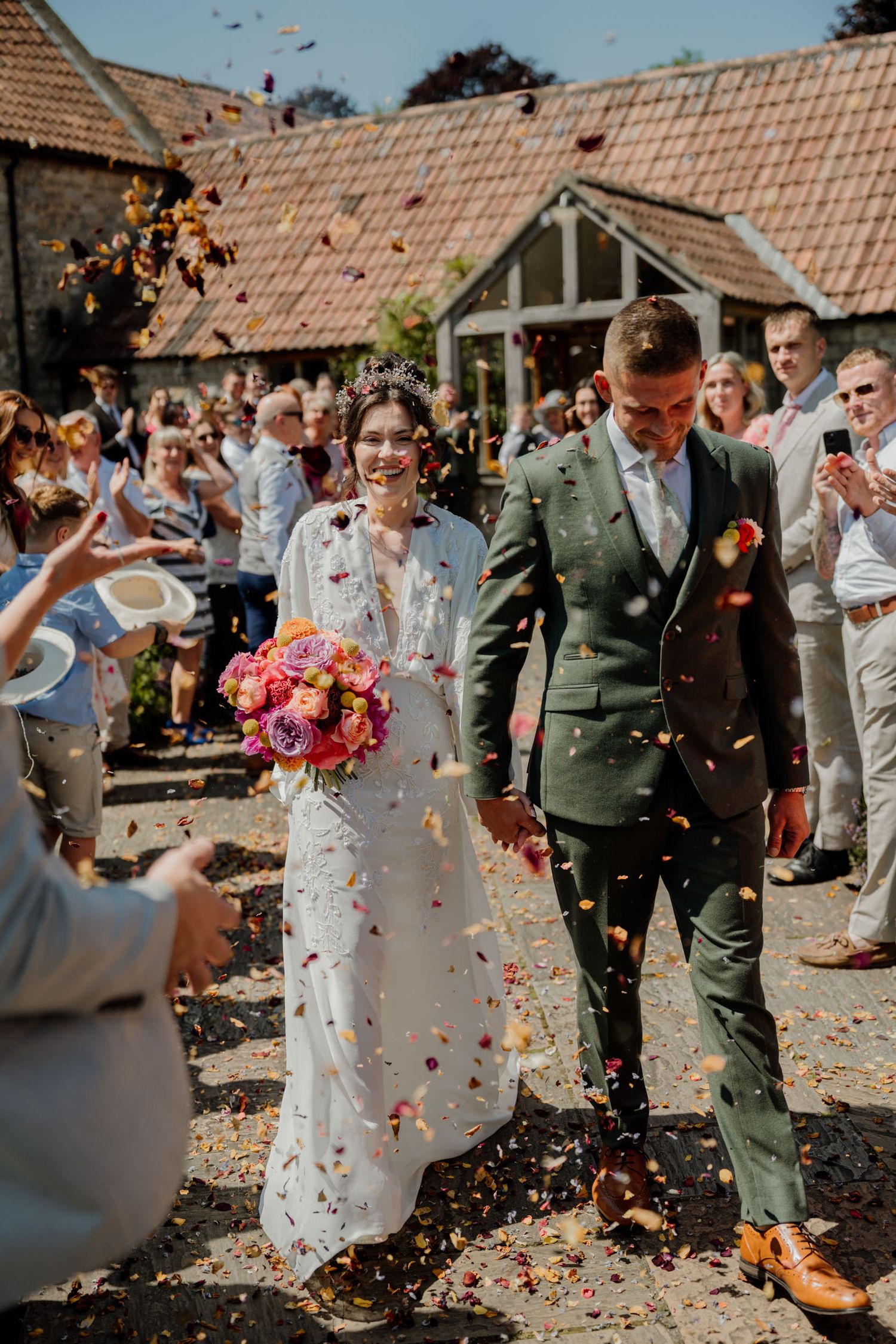 Celebratory moment with confetti being thrown over wedding couple outside brick building on sunny day.