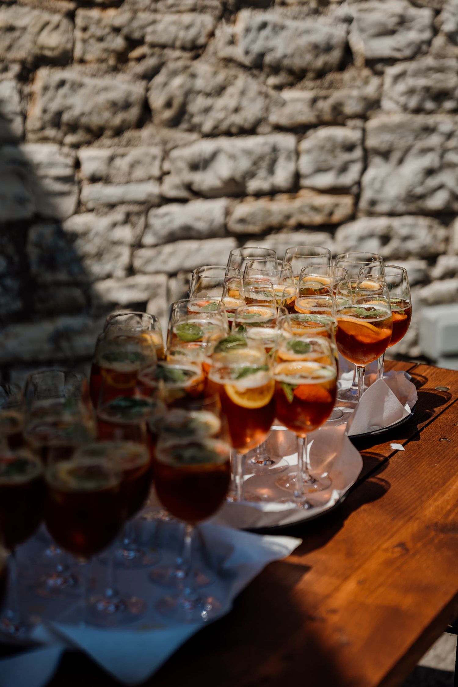 Elegant cocktail glasses filled with amber-colored drinks arranged on a rustic wooden surface against a stone wall.