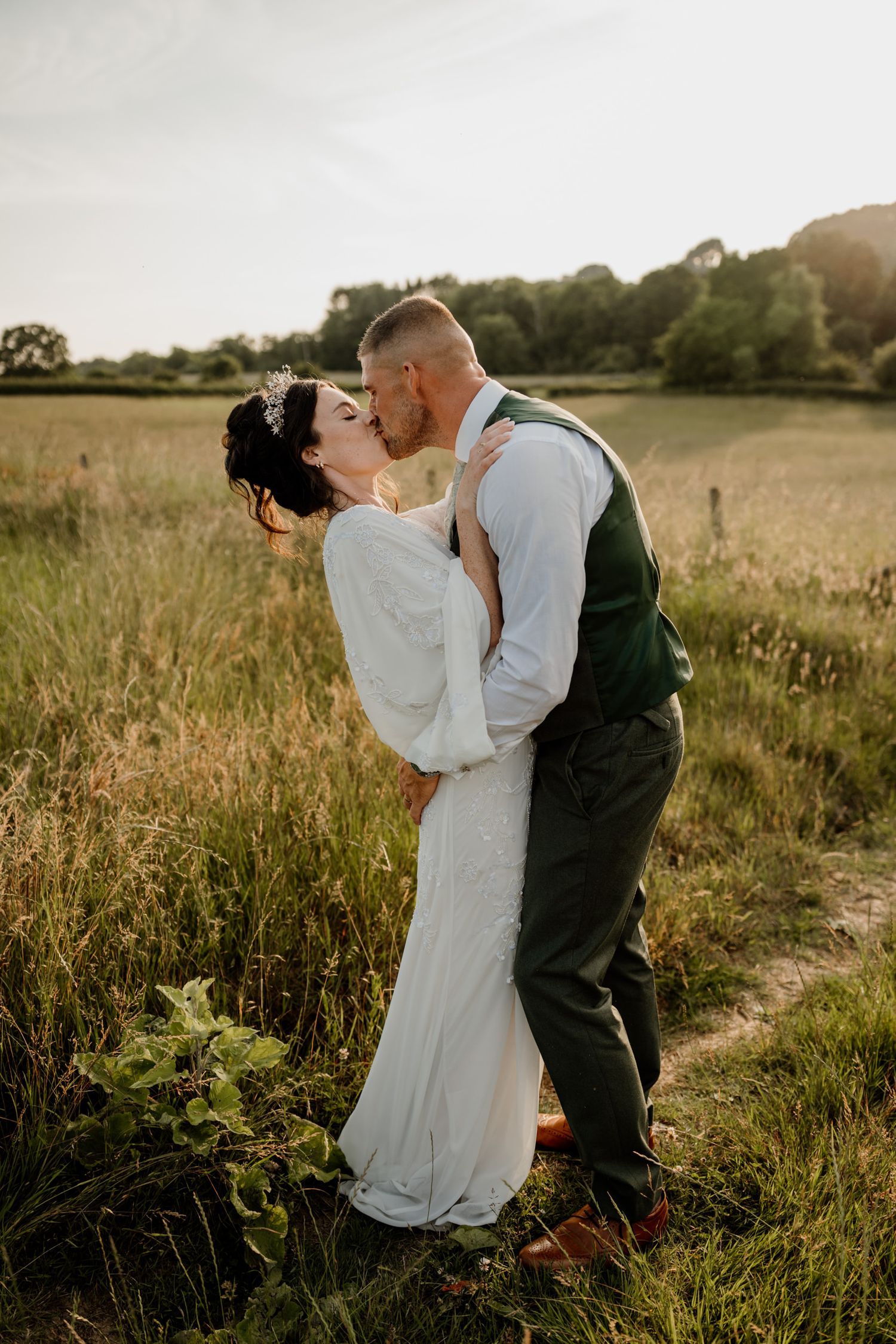 Intimate wedding couple moment photographed in a sunlit meadow at golden hour.