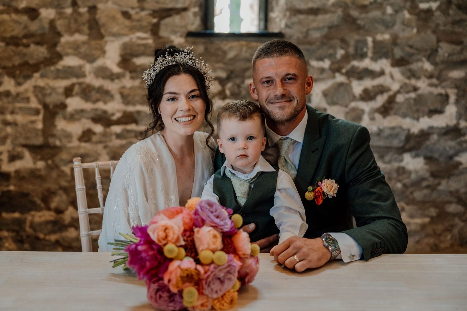 Three wedding photos showing people with vibrant floral arrangements in a rustic stone wall setting during a celebration.