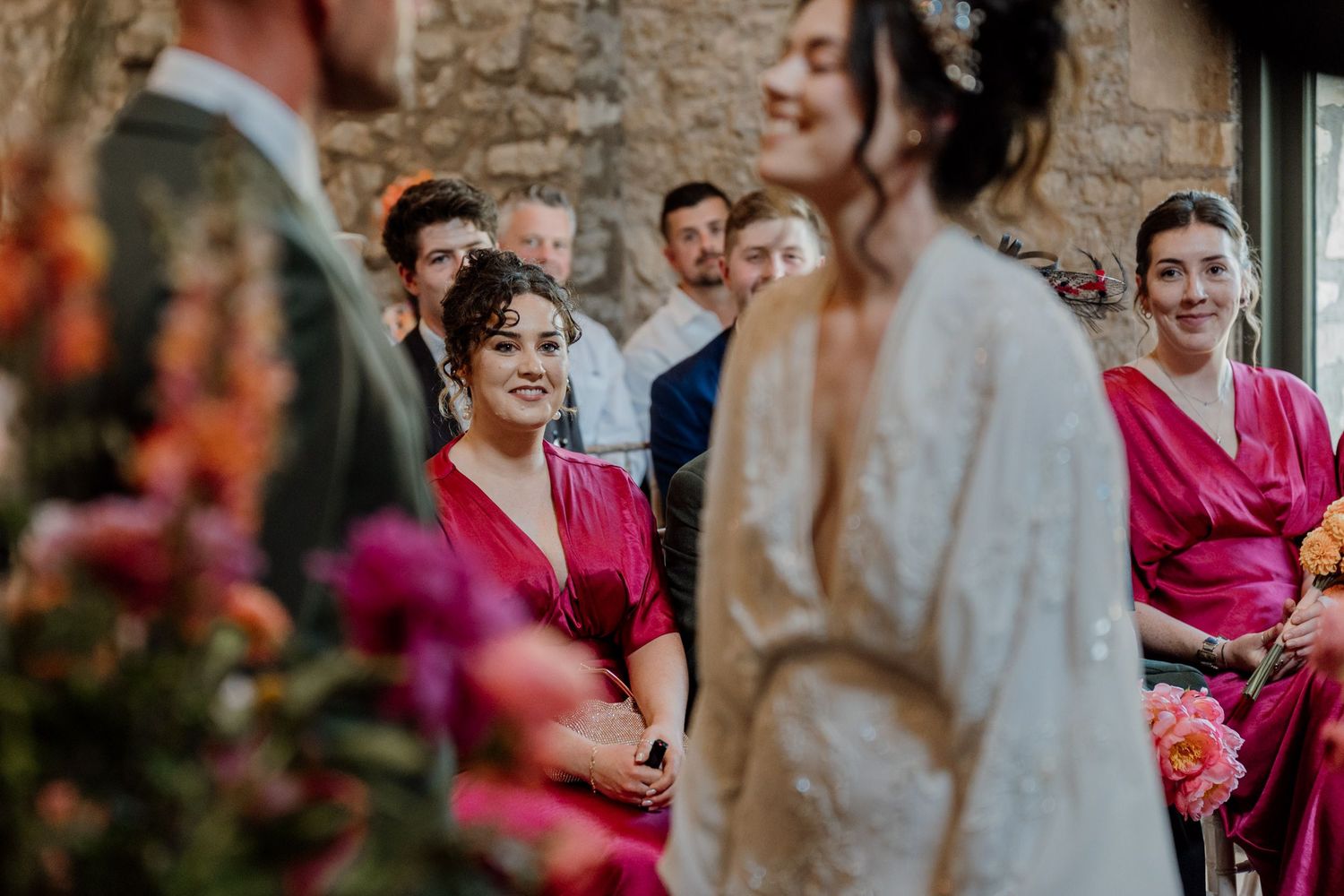 Wedding party dressed in pink and burgundy outfits celebrate joyfully in an outdoor setting.