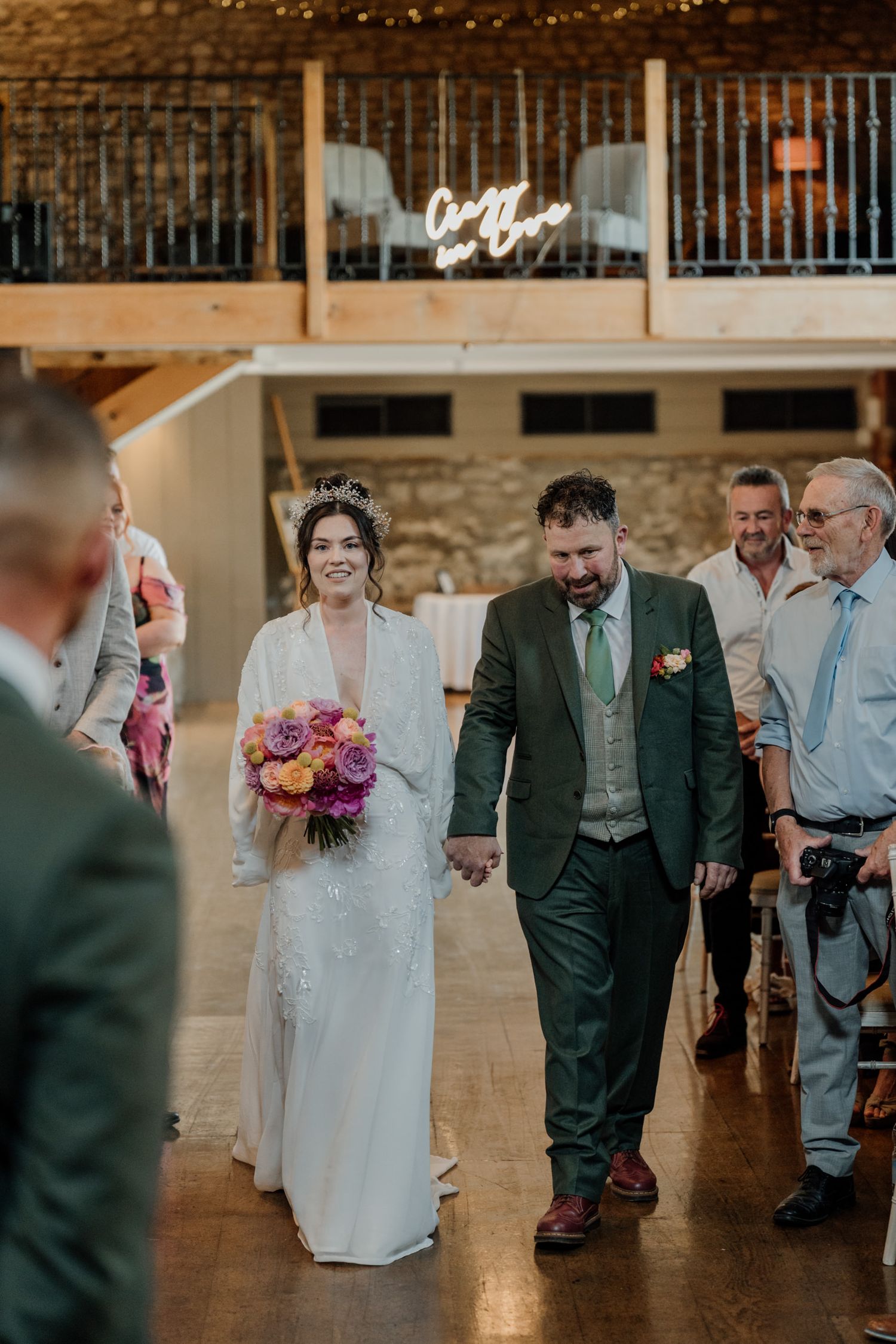 Wedding guests gather in an elegant indoor venue with stone walls and warm lighting.