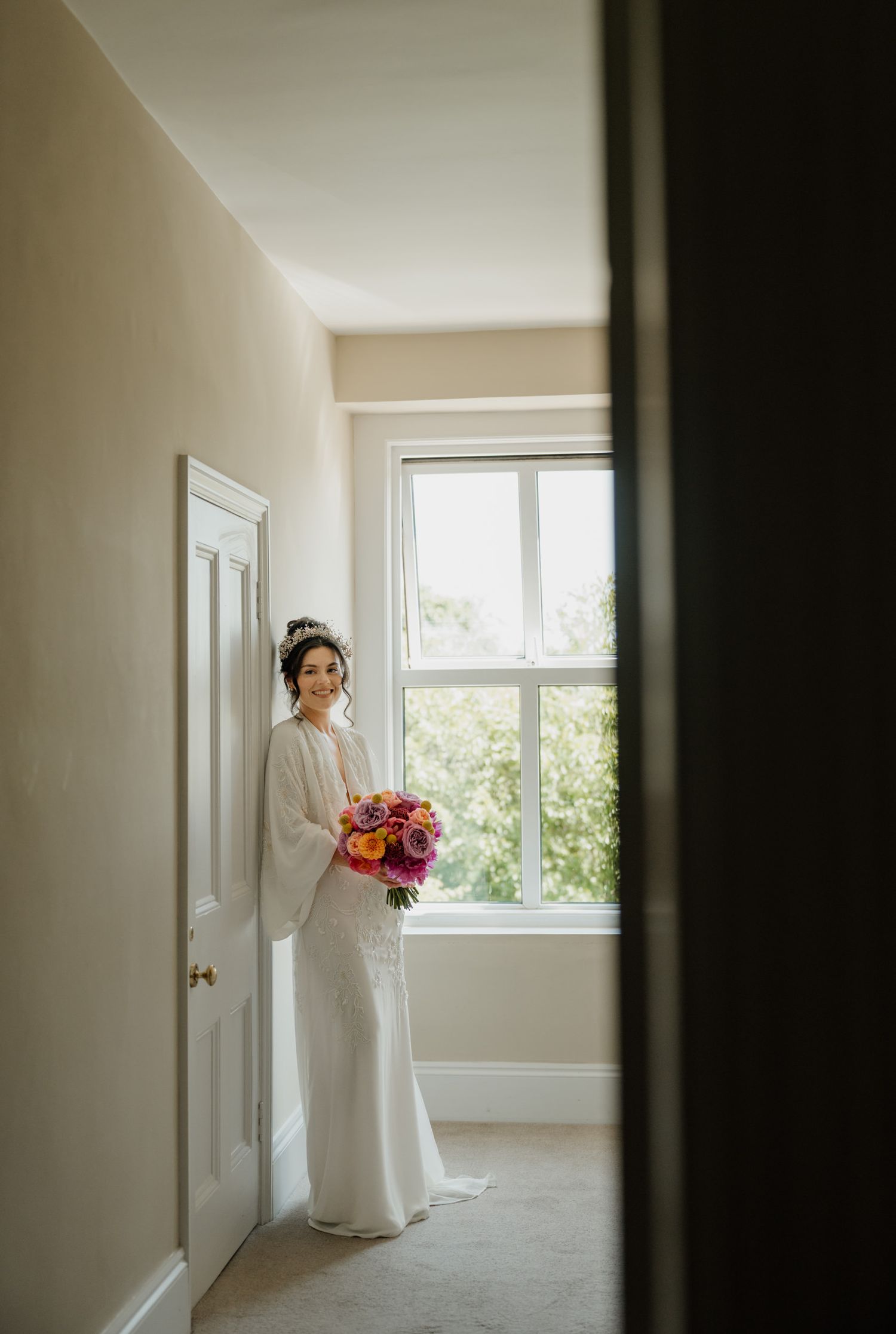Minimalist white room with natural light streaming through windows and wedding dress preparation.