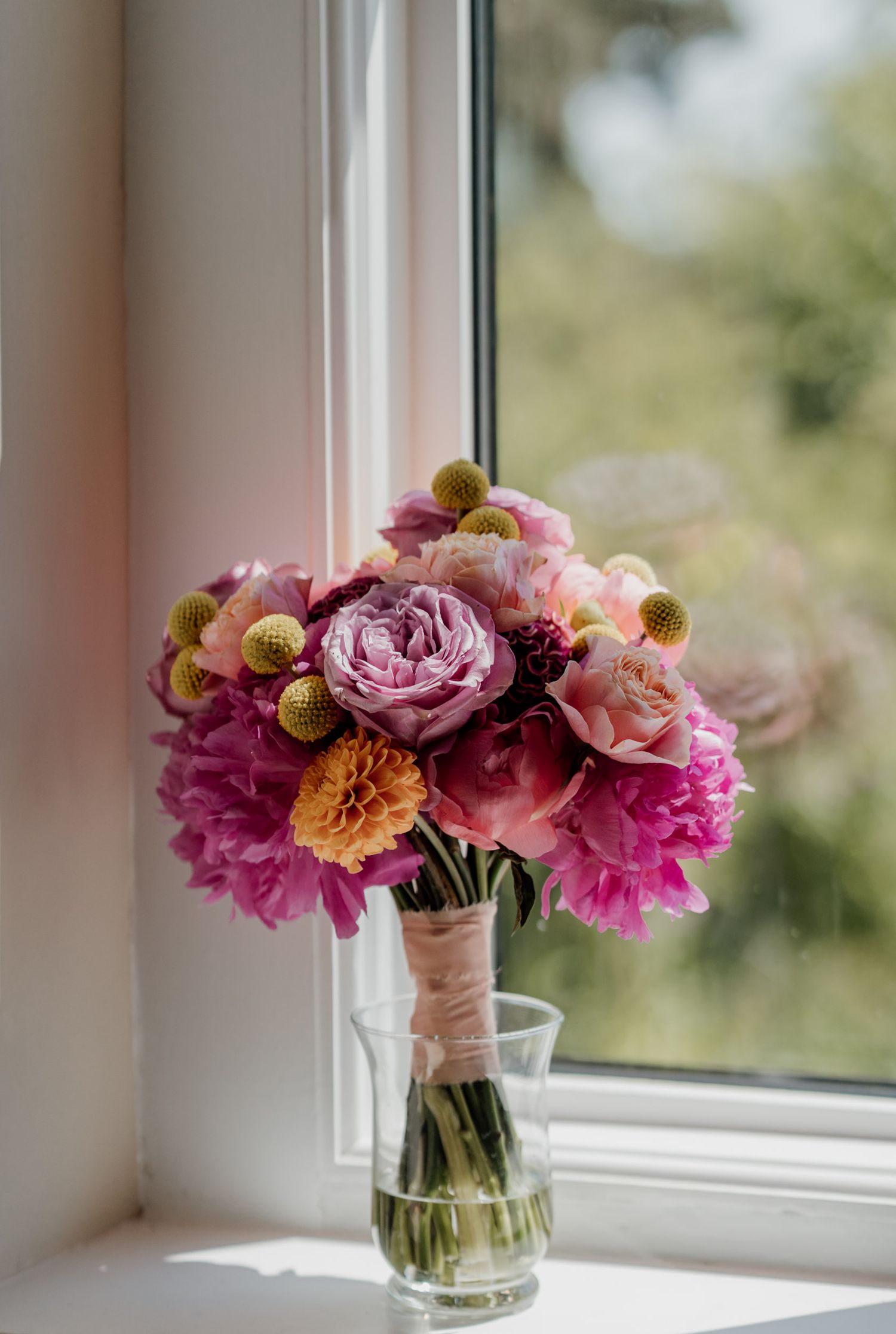 Pink and purple floral arrangement with peonies and dried flowers sits on a bright windowsill.
