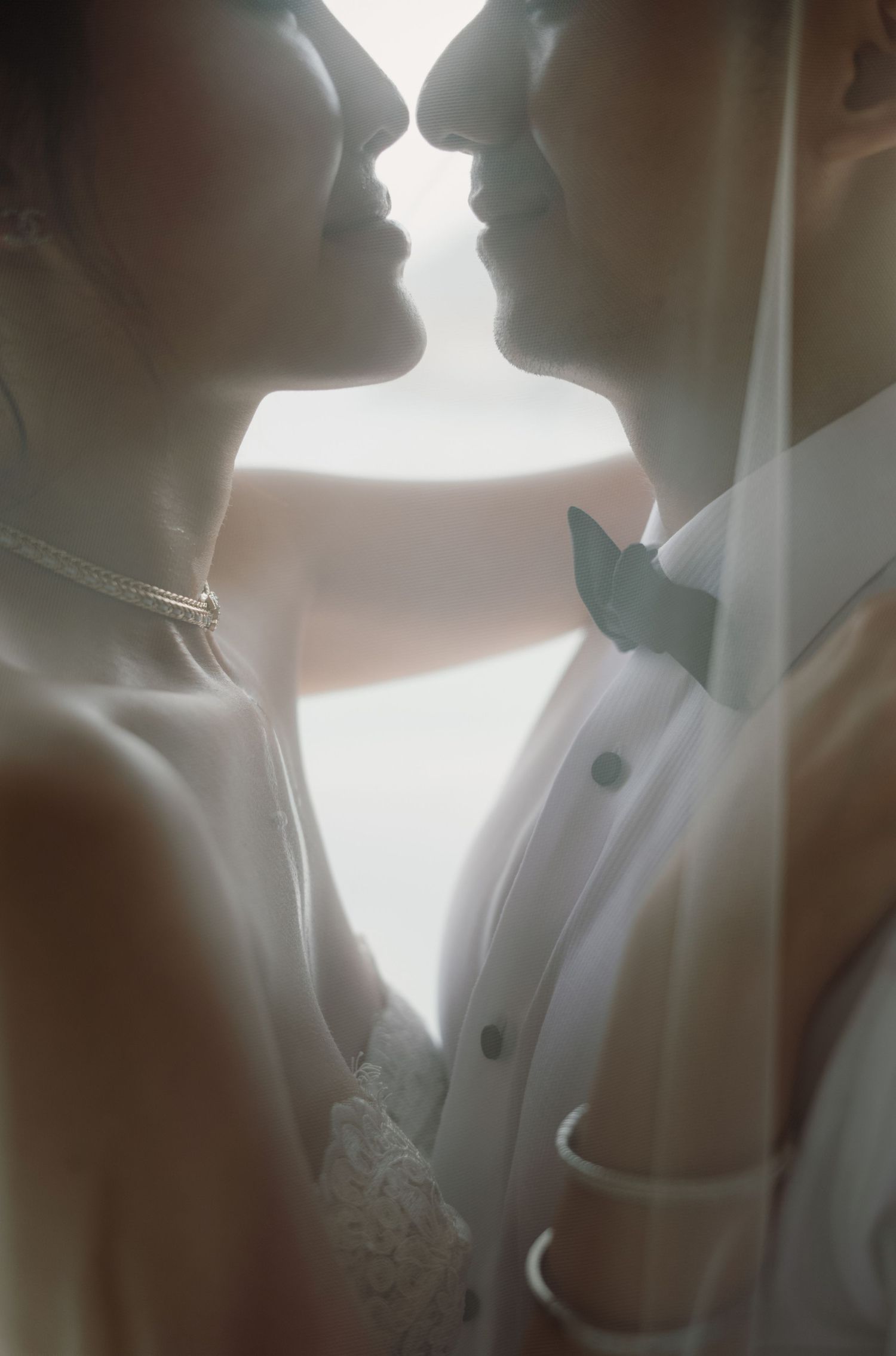 Silhouetted profiles of a bride and groom sharing an intimate moment in soft, romantic lighting.