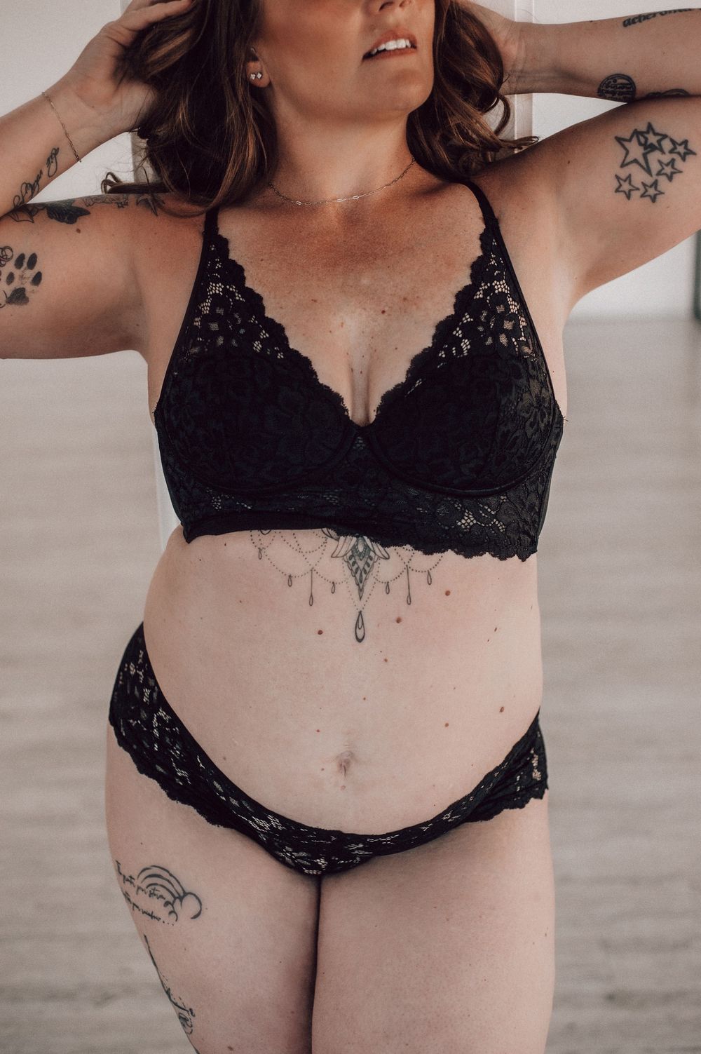Woman in black lace bralette and matching bikini bottoms with tattoos posing confidently.