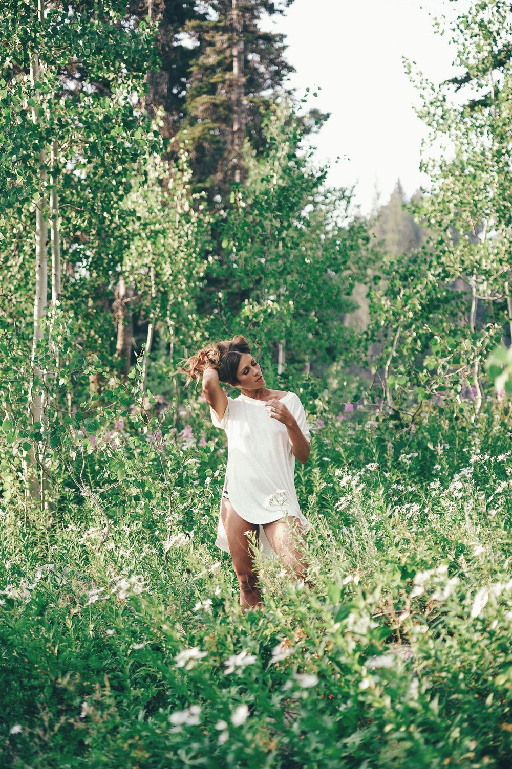 Fashion photography in lush green forest with sunlight filtering through trees.