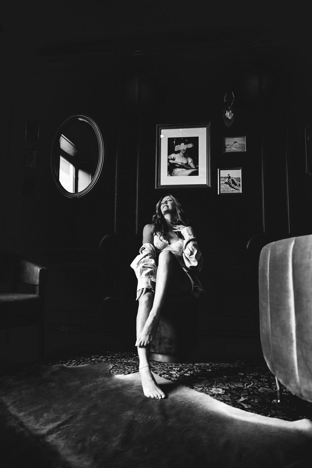 Artistic black and white portrait in moody room interior with oval mirror.