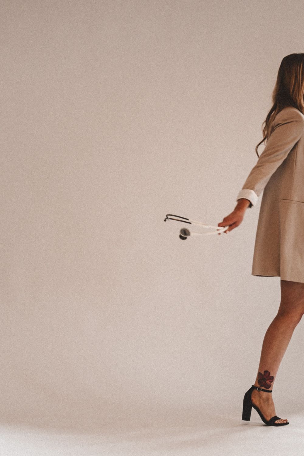 Elegant figure in beige coat and heels against neutral background.