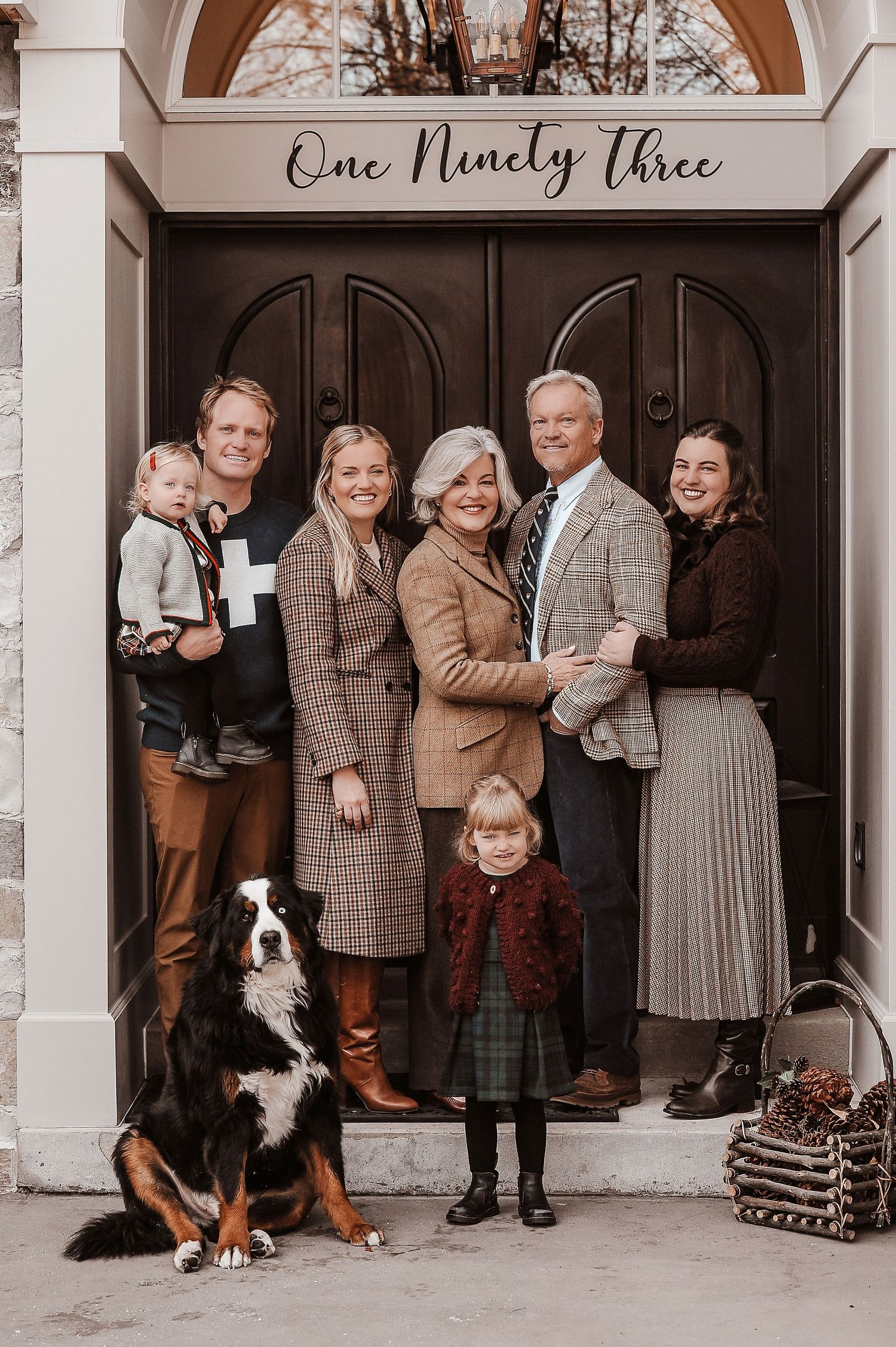 Vintage-styled family group portrait with dog in front of building entrance.