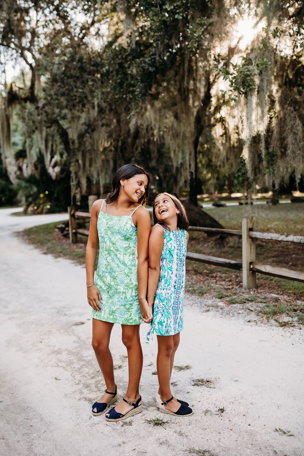 Two children in matching summer outfits stand together on a sandy path surrounded by Spanish moss draped trees.