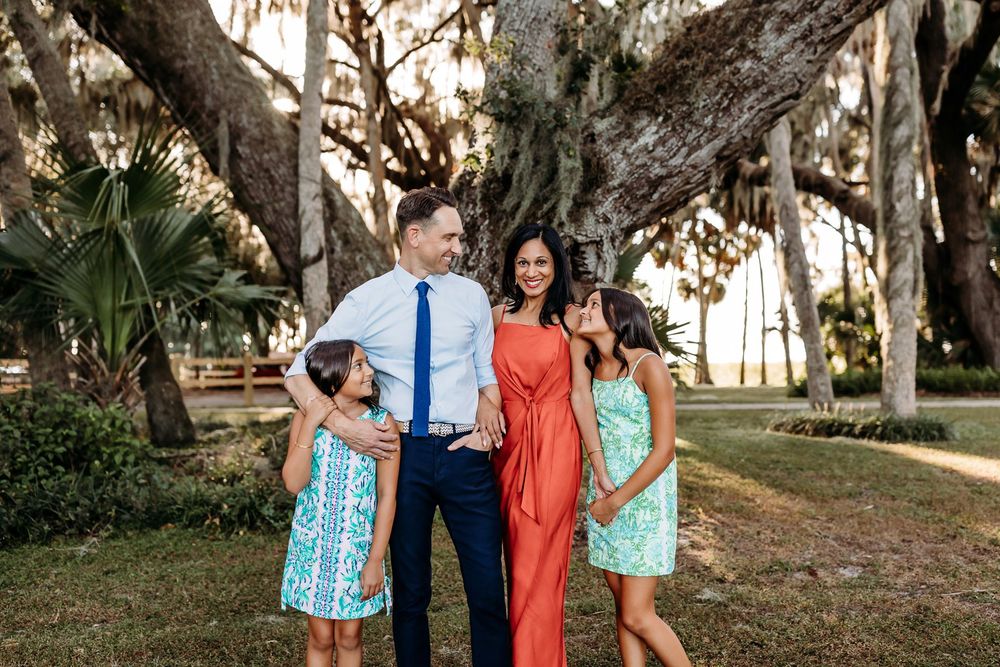A group of people pose together under large trees during an outdoor photo session at sunset.