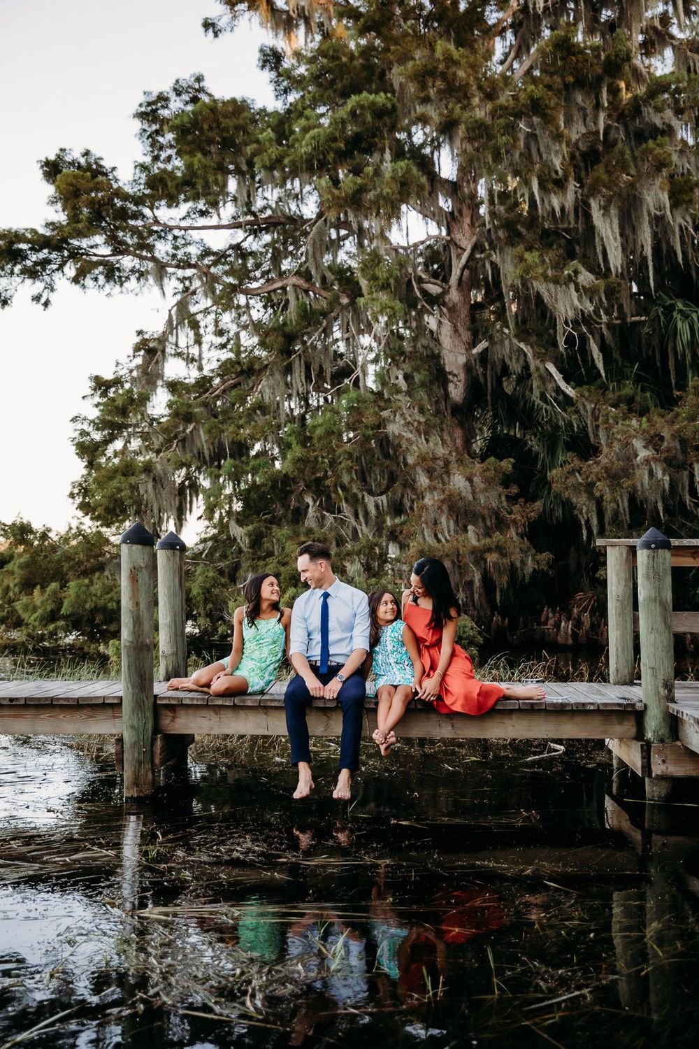 A group sits together on a wooden dock overlooking a serene waterway with Spanish moss hanging from trees.