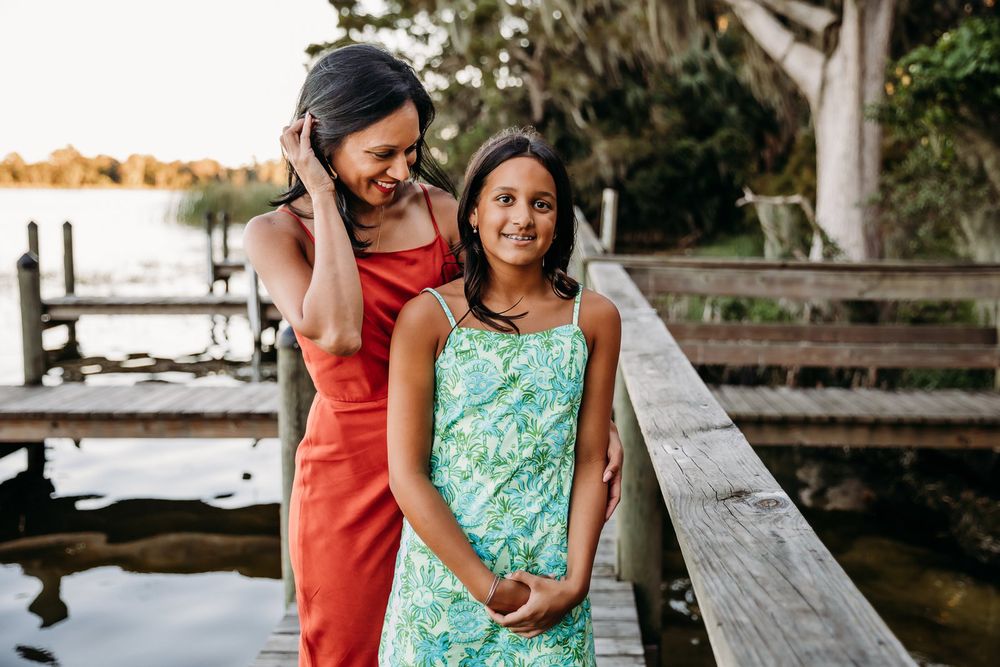 Two people in colorful dresses share a joyful moment together on a wooden dock by the water at sunset.