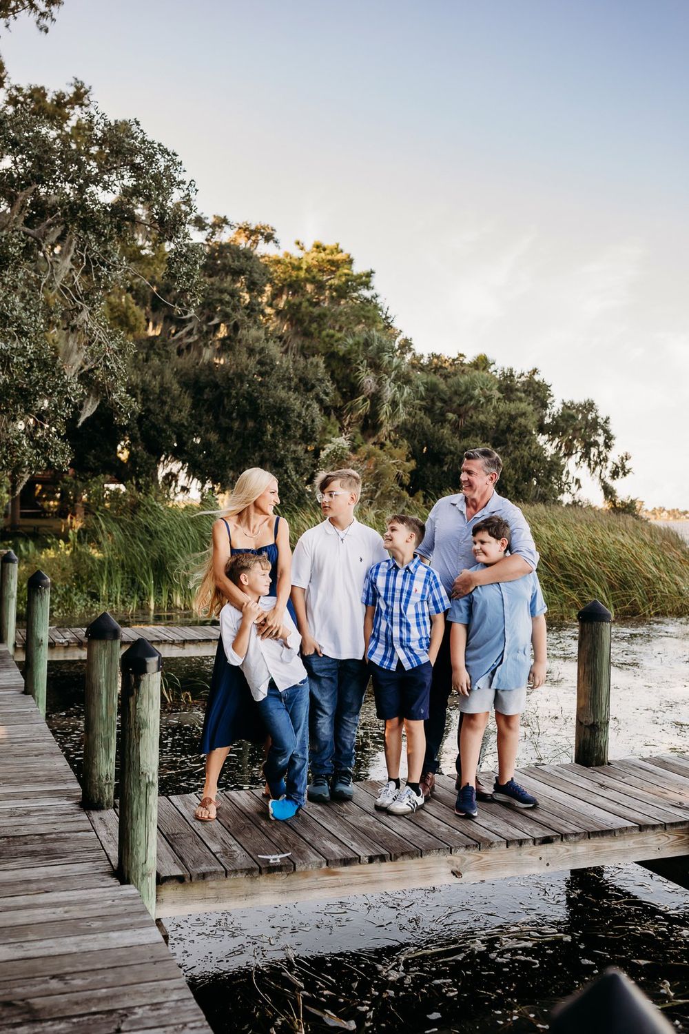 Group sits casually along a wooden dock at sunset with Spanish moss trees in the background.