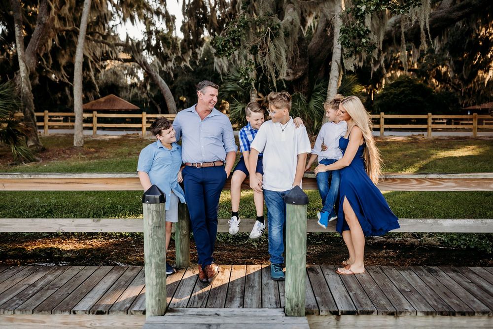 Family members relax and laugh together on a rustic wooden pier by the water.