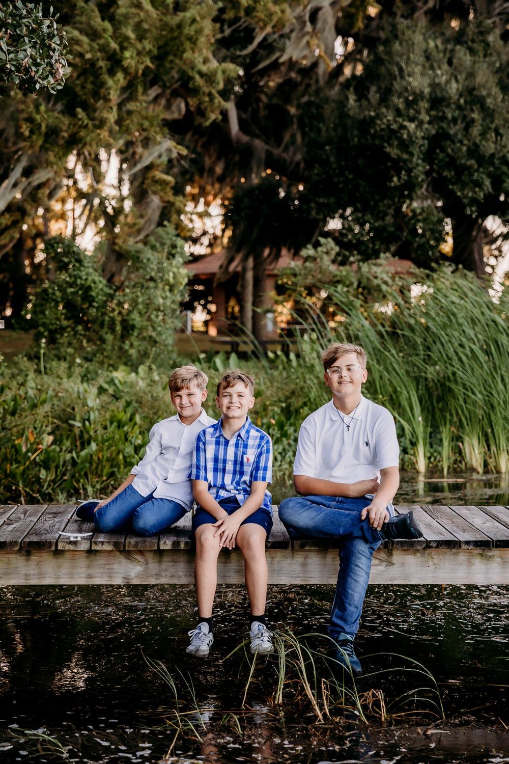 Three young people sit on wooden boardwalk near tall marsh grasses at golden hour.