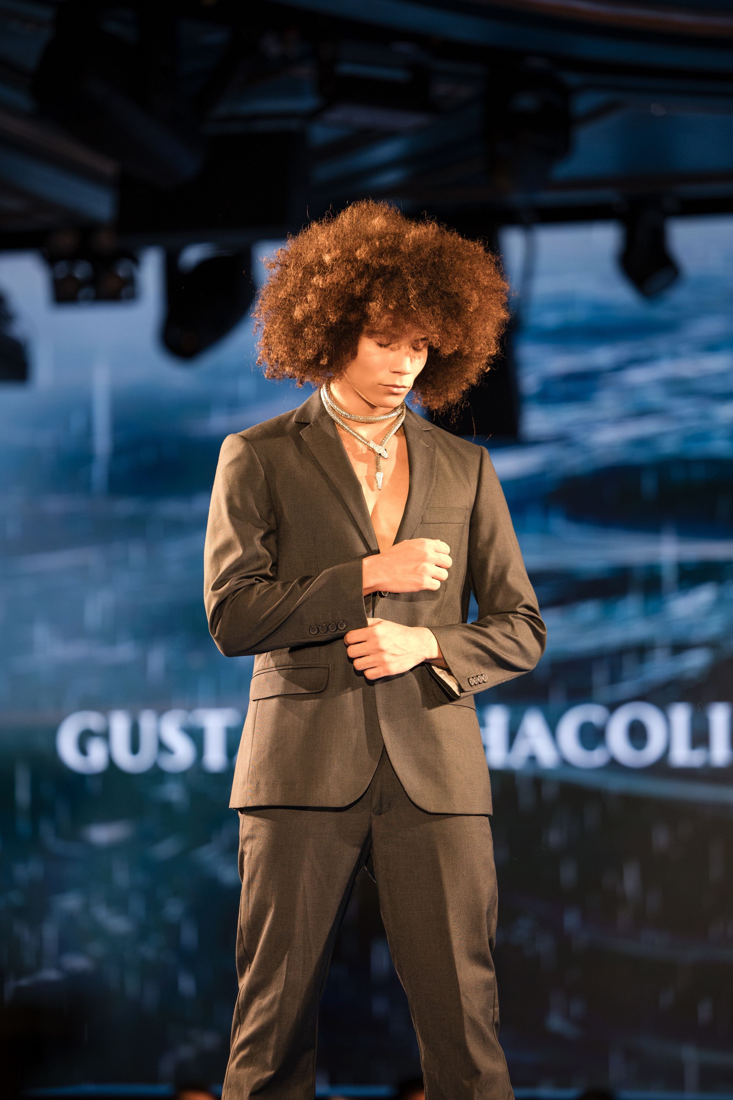 Performer in black suit jacket poses dramatically on dimly lit stage.