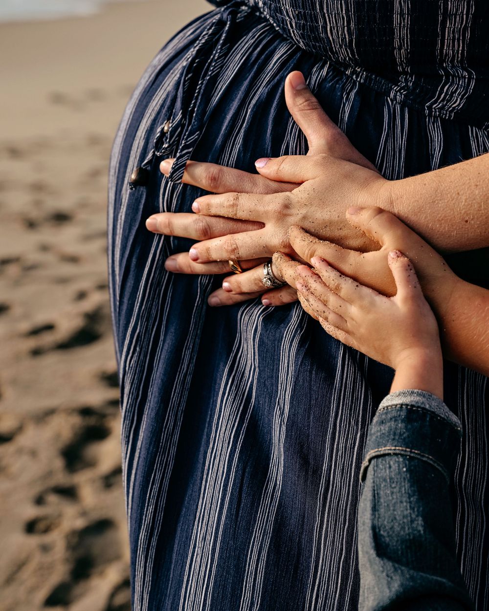 Close-up detail shots of pregnant belly and hands against navy blue fabric on sandy beach.
