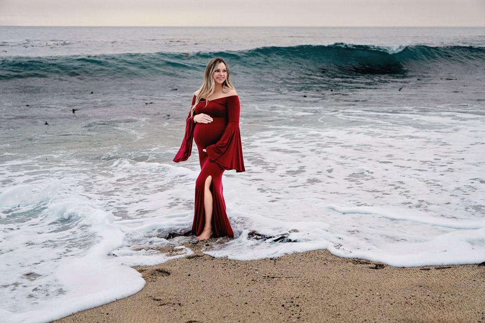 A figure in a flowing red dress walks along a dramatic coastline with crashing waves.