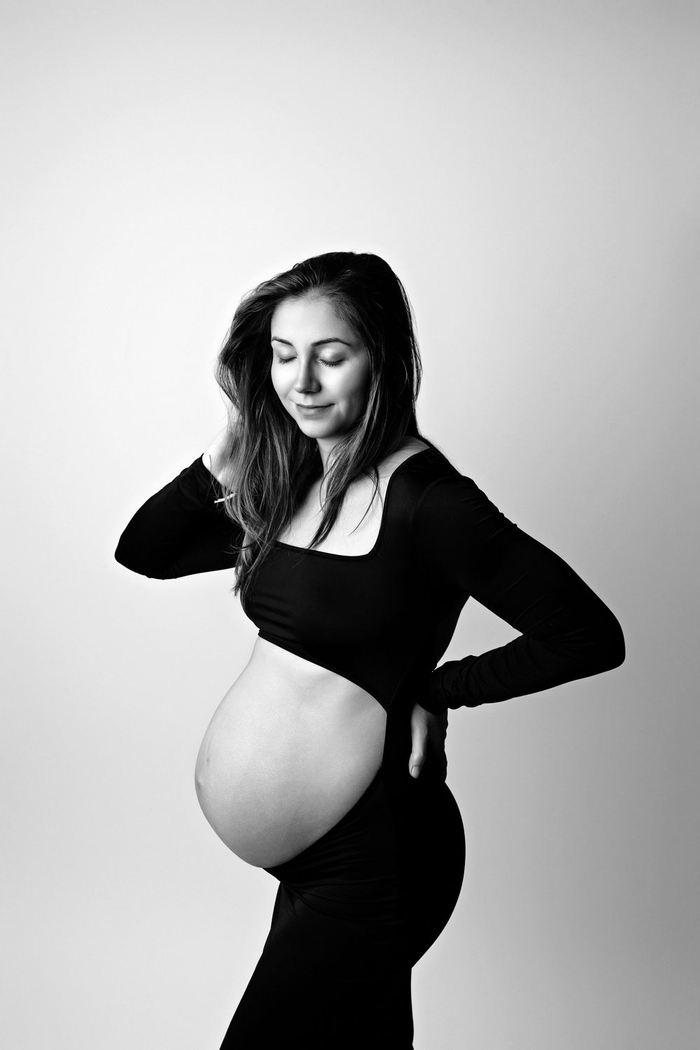 A black and white maternity photoshoot shows an expectant mother in three artistic poses wearing a black dress.