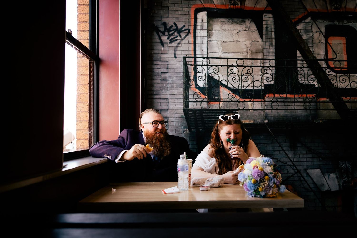 A wedding party poses for candid photo reactions at a rustic venue with brick walls and wrought iron details.