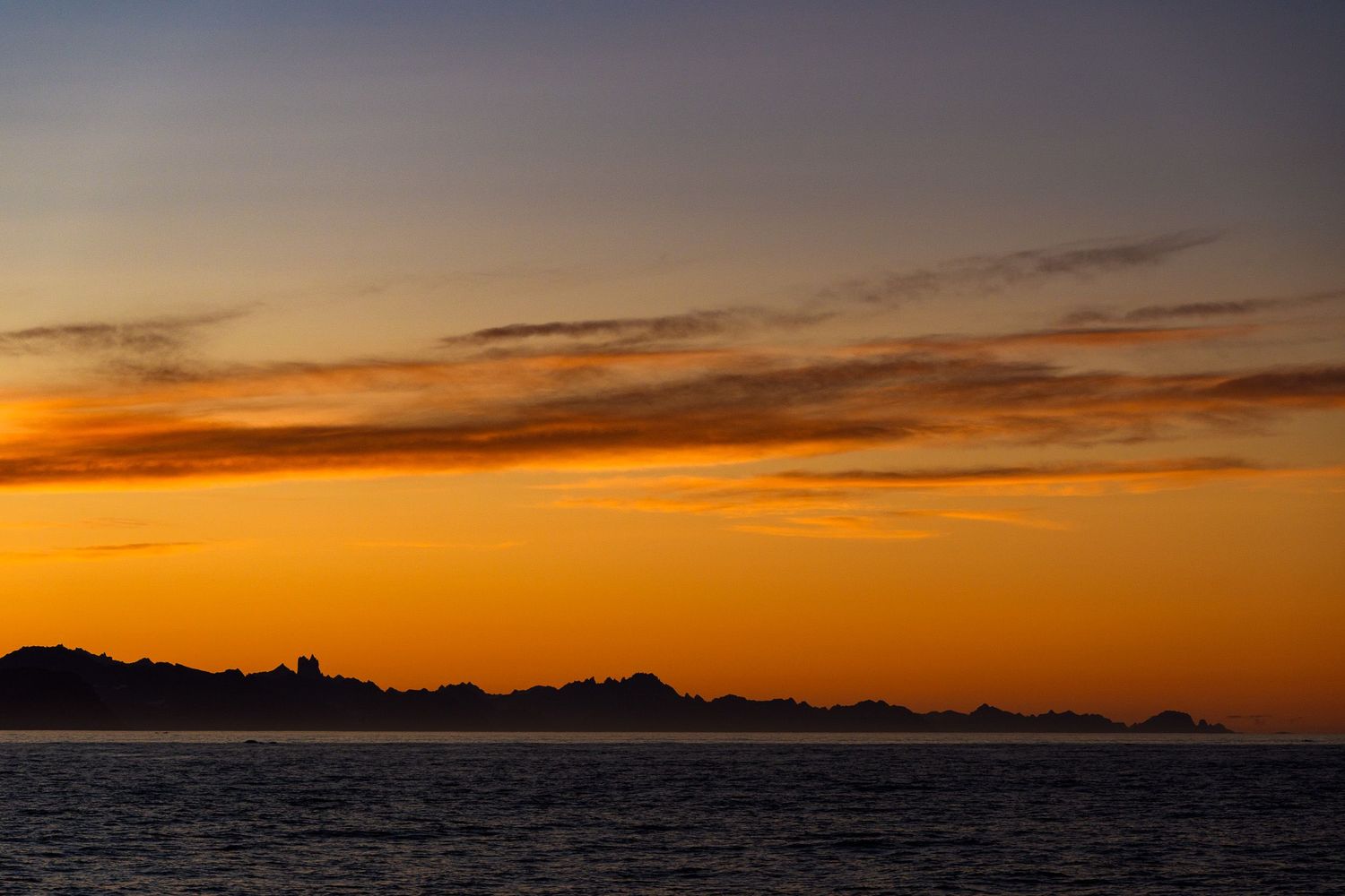 Stunning panoramic sequence of orange and golden sunset sky over silhouetted mountains and ocean horizon.