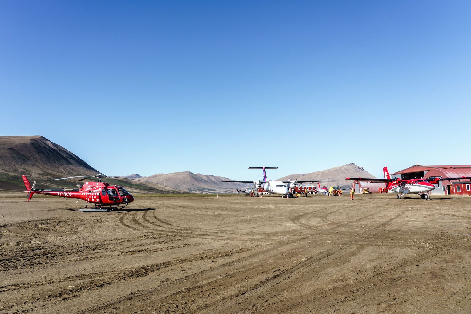Several red rescue helicopters parked in a desert landscape with brown terrain and mountains in the background.