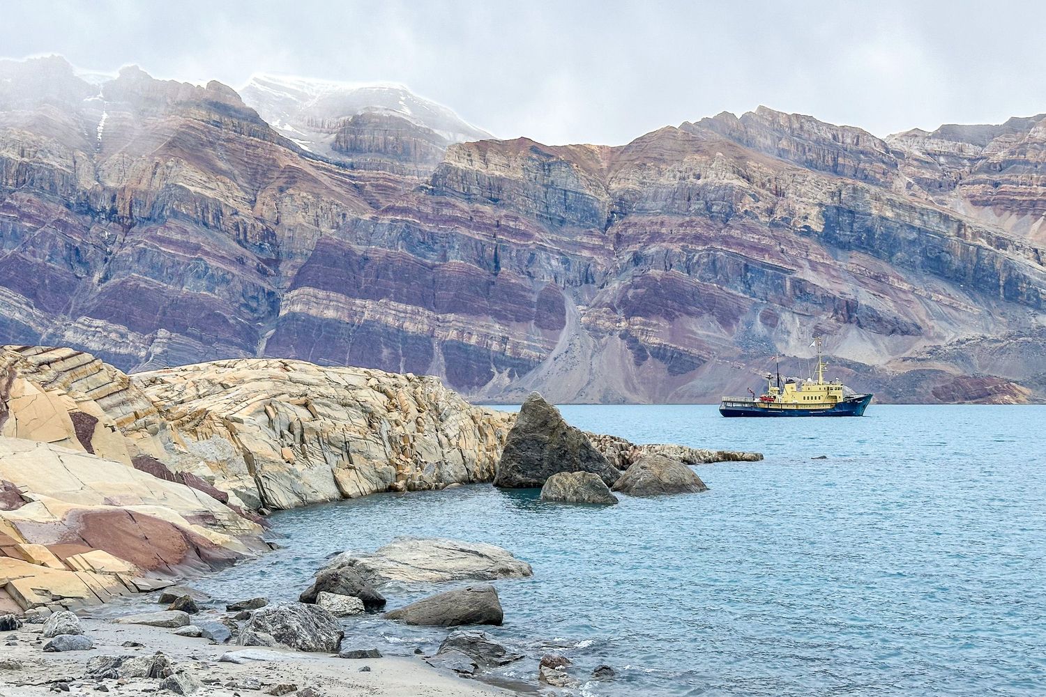 Panoramic view of rugged cliffs and blue waters along a rocky coastline with mountains in the background.